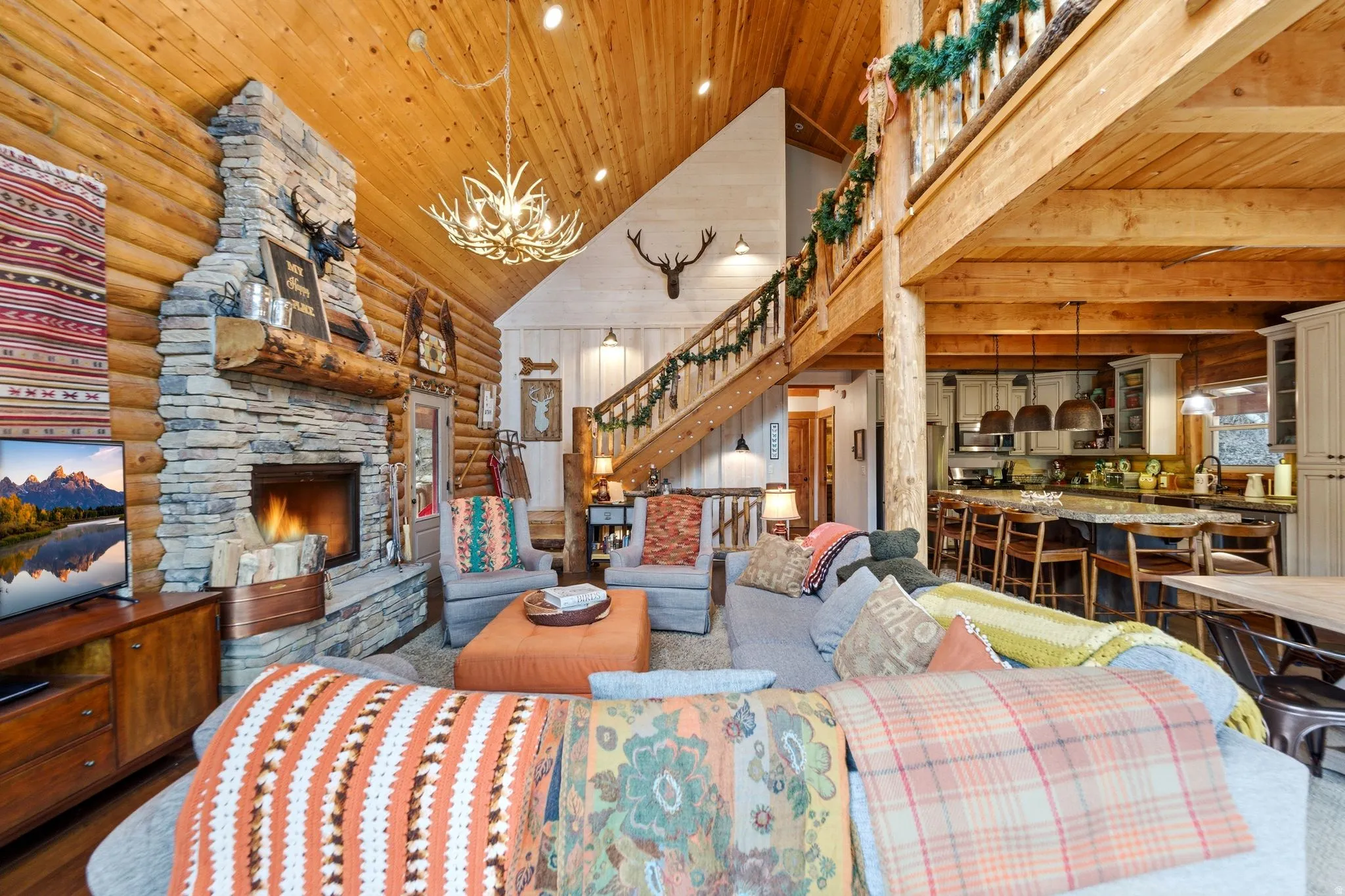 Living area with a vaulted wood ceiling, a stone fireplace, rustic walls, and hanging lights