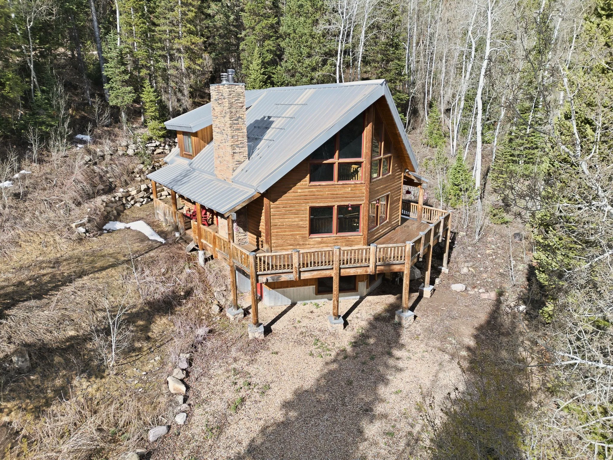 View of front facade featuring a chimney, a metal roof, a wooden deck, and a wooded view