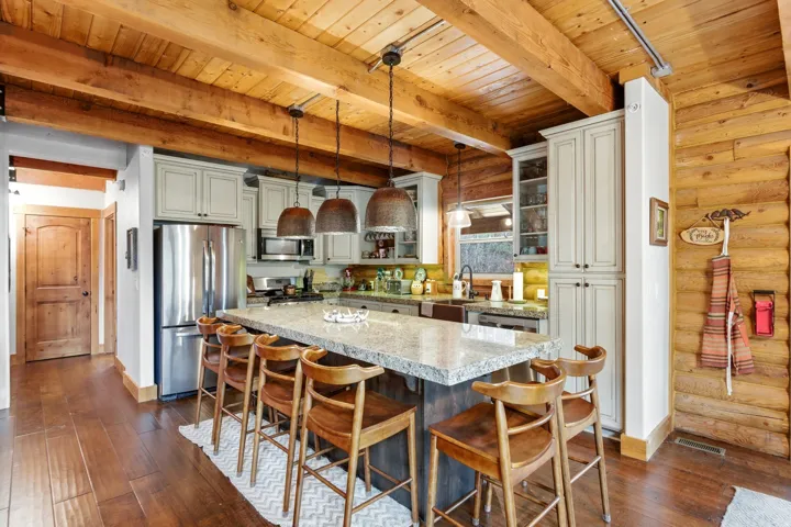 Kitchen featuring stainless steel appliances, pendant lighting, dark wood finished floors, light stone counters, and rustic walls