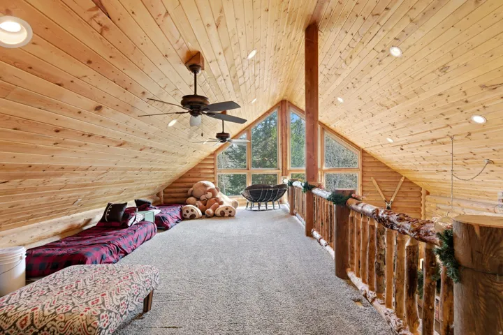 Living area featuring log walls, wooden ceiling, carpet flooring, and a ceiling fan