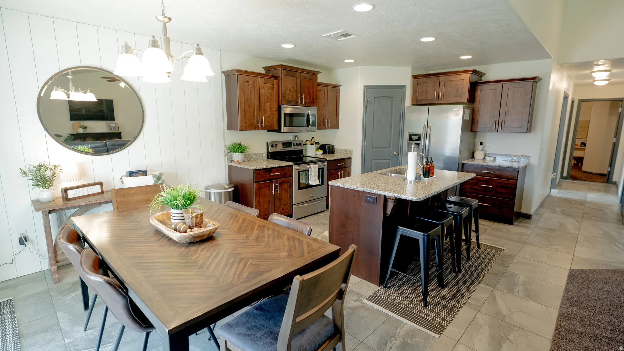 Kitchen featuring stainless steel appliances, light stone counters, a kitchen island with sink, hanging lights, and a breakfast bar area