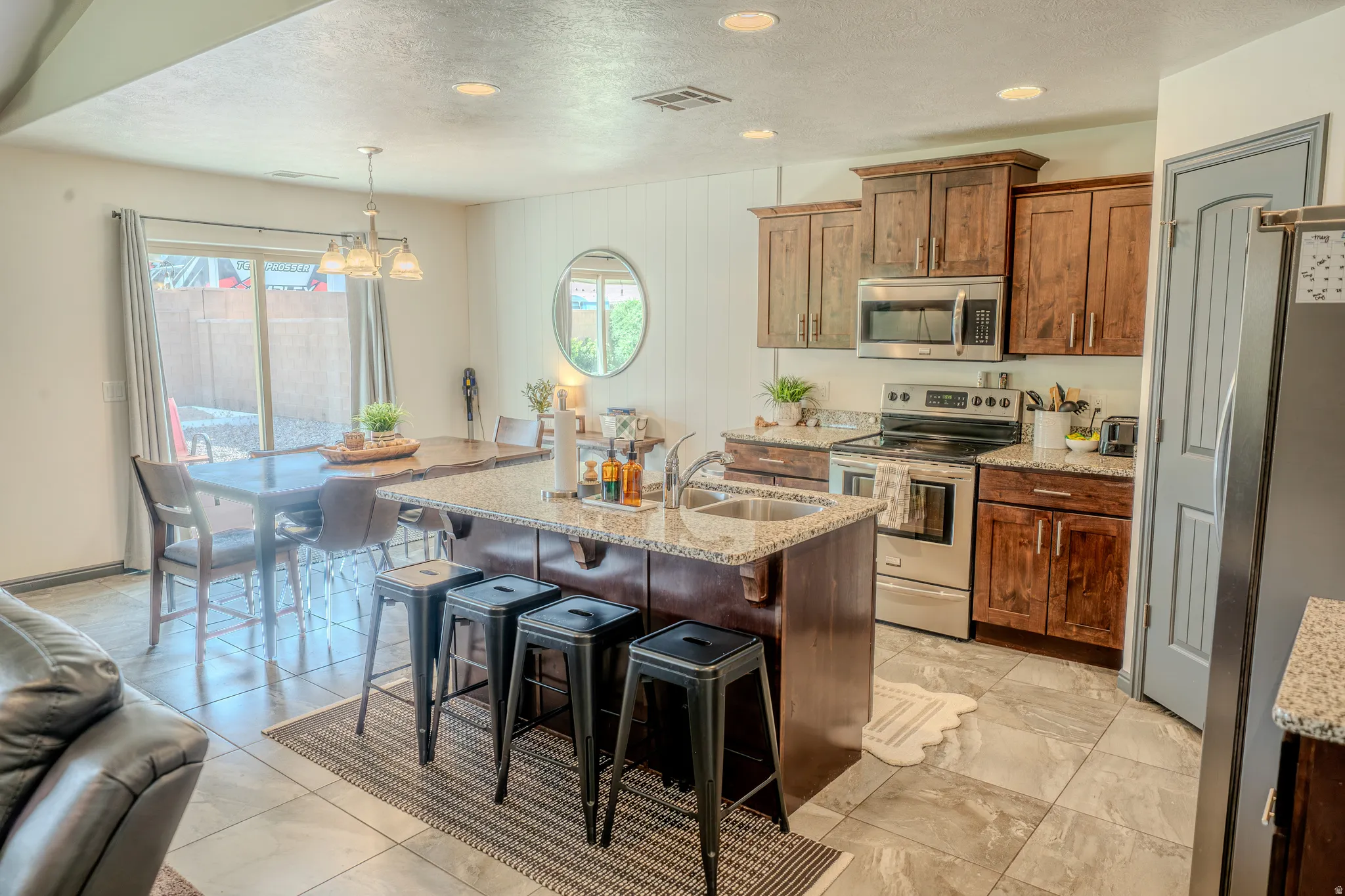 Kitchen featuring stainless steel appliances, a textured ceiling, light stone counters, a kitchen island with sink, and a breakfast bar