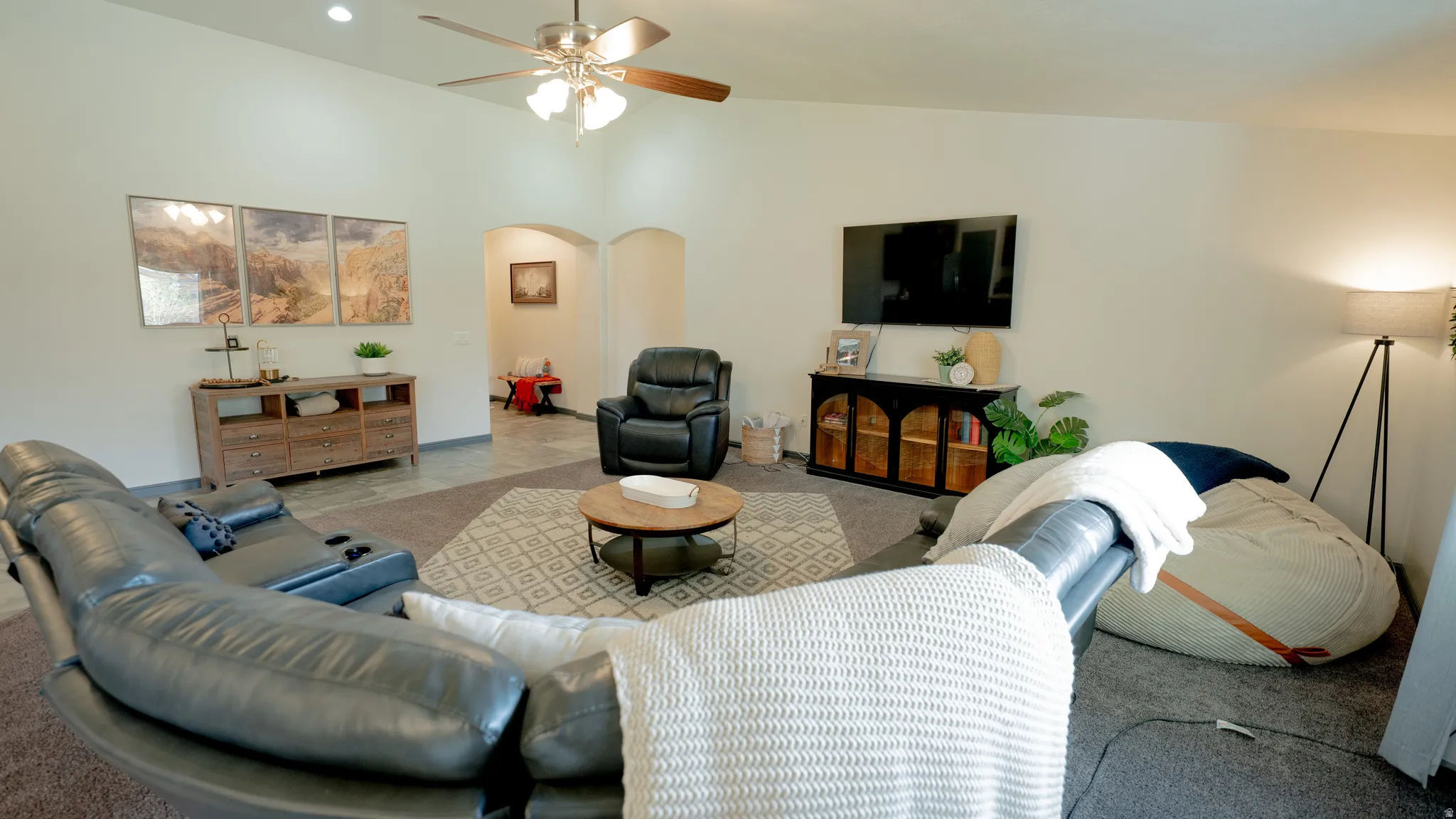 Carpeted living area with arched walkways, ceiling fan, and vaulted ceiling