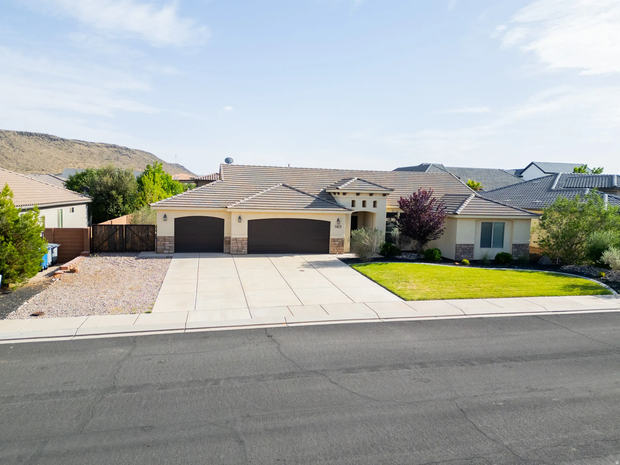 View of front of property featuring an attached garage, stucco siding, stone siding, and a gate