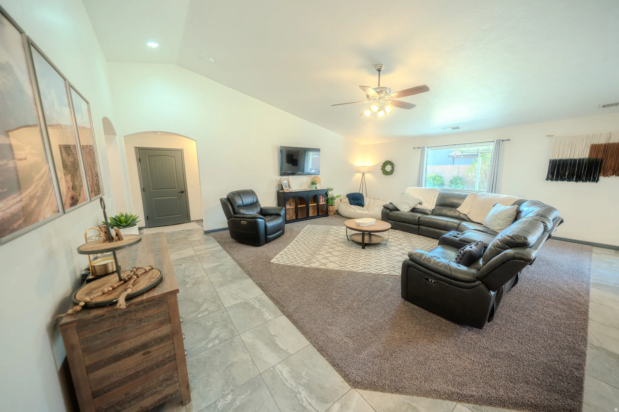 Living area featuring arched walkways, light colored carpet, ceiling fan, lofted ceiling, and light tile patterned flooring