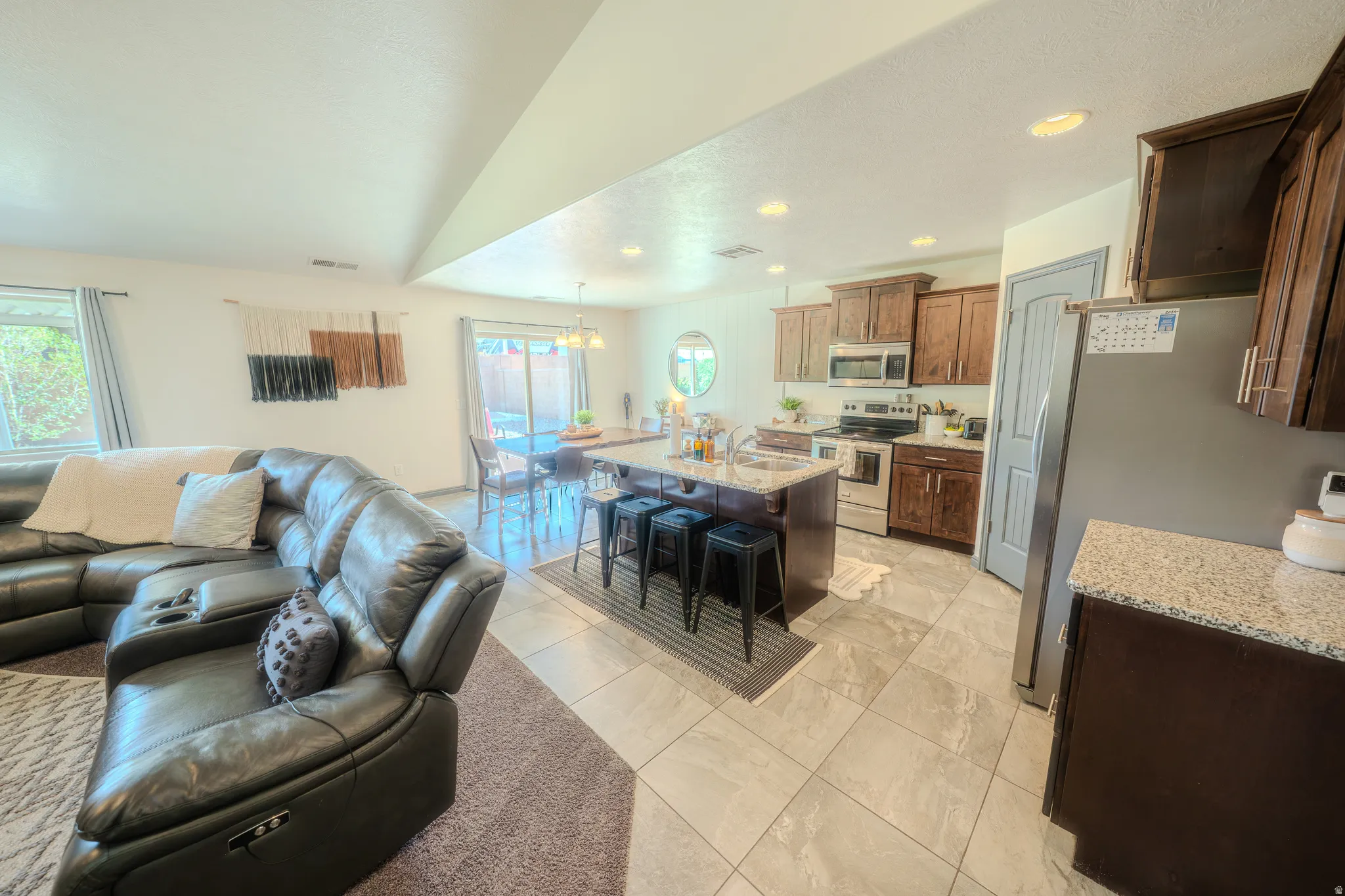 Kitchen with open floor plan, stainless steel appliances, a kitchen bar, light stone countertops, and an island with sink