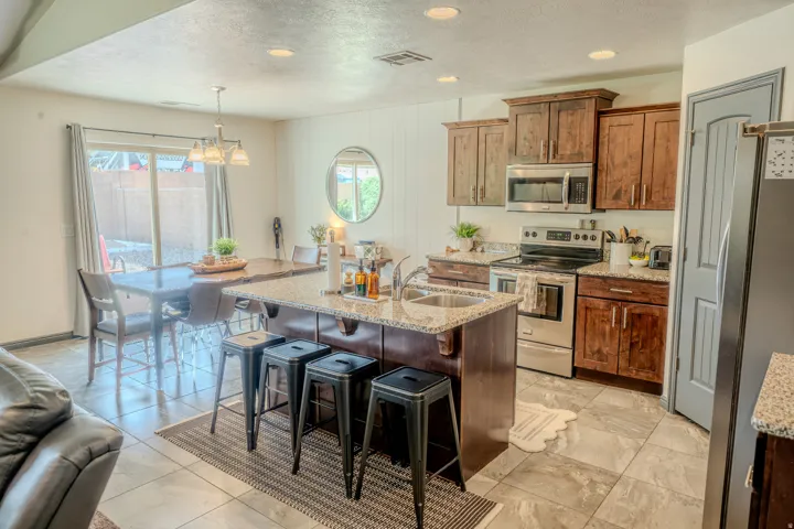 Kitchen featuring stainless steel appliances, a textured ceiling, light stone counters, a kitchen island with sink, and a breakfast bar