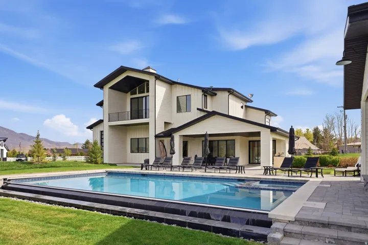 Rear view of property with a lawn, a patio area, a balcony, a pool with connected hot tub, and a mountain view