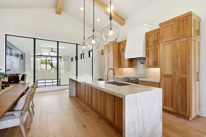 Kitchen with light stone countertops, a large island with sink, tasteful backsplash, light wood finished floors, and pendant lighting