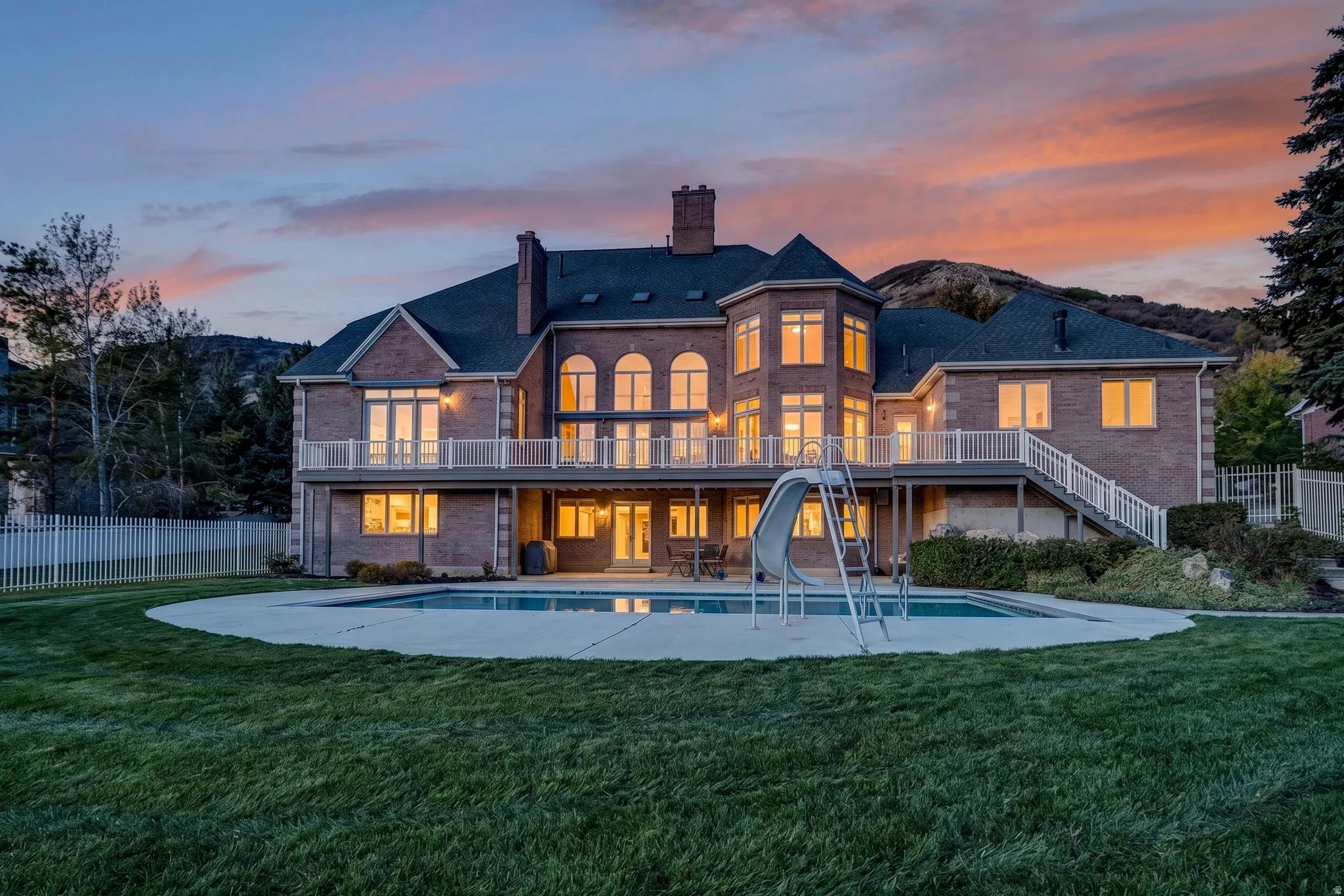 Back of property at dusk with a chimney, a patio area, brick siding, and a balcony