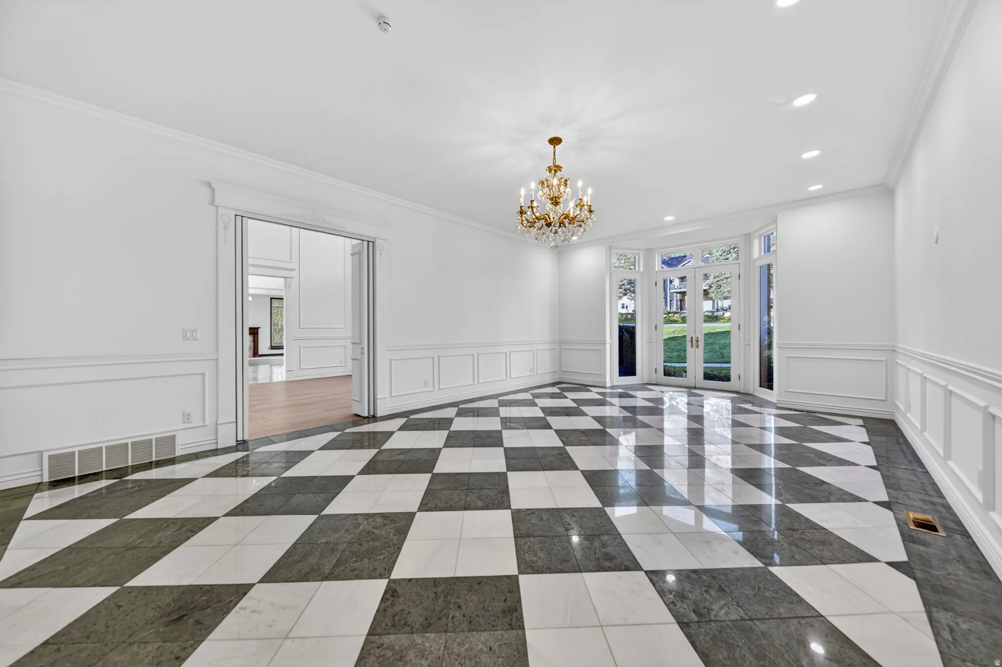 Dining room featuring chandelier and recessed lighting, a decorative wall, ornamental molding, marble and inlaid floor details, and wainscoting