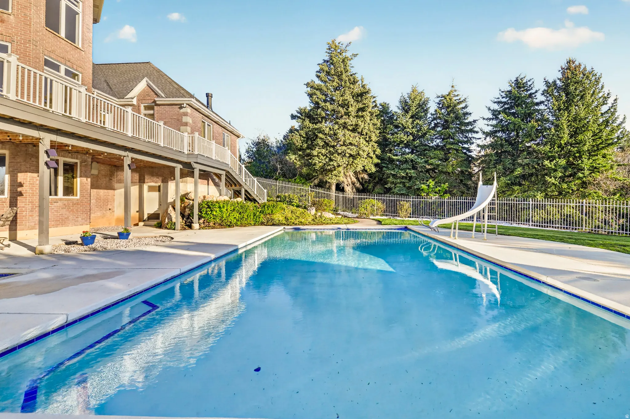 View of swimming pool featuring patio surround, a water slide, and a balcony