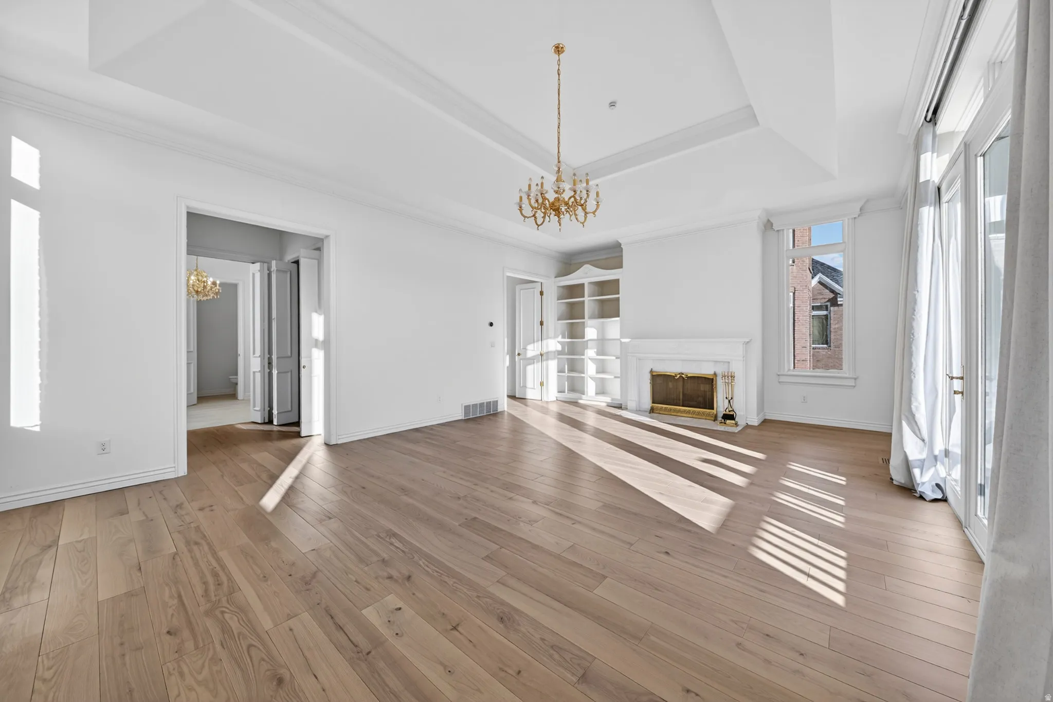 Primary suite featuring chandelier, hardwood floors, built in features, a high end fireplace, and ornamental molding