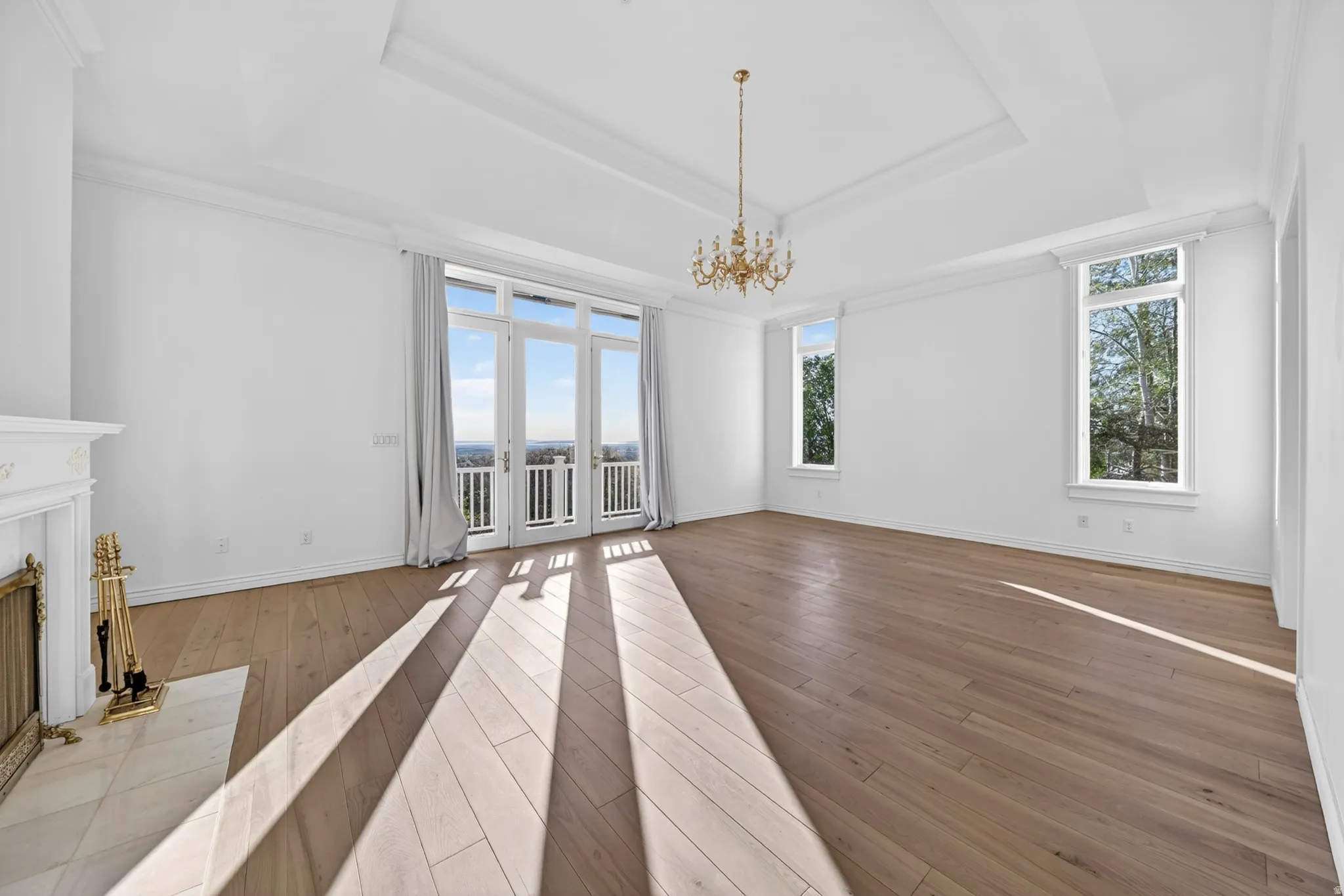 Primary suite featuring hardwood floors, a chandelier, a high end fireplace, ornamental molding, and a tray ceiling