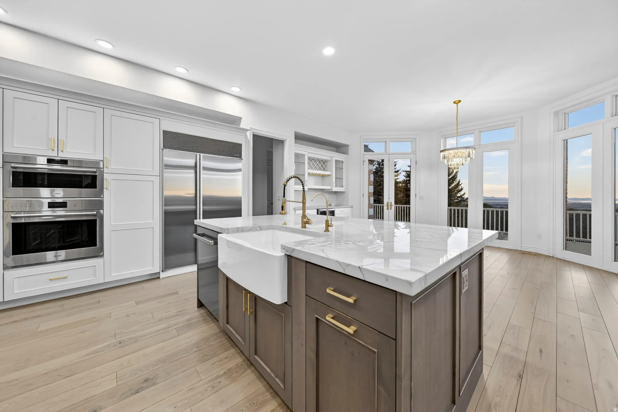 Kitchen with two tone cabinets, a center island with sink, stone counters, Wolf and Sub-Zero stainless steel appliances, and hardwood flooring