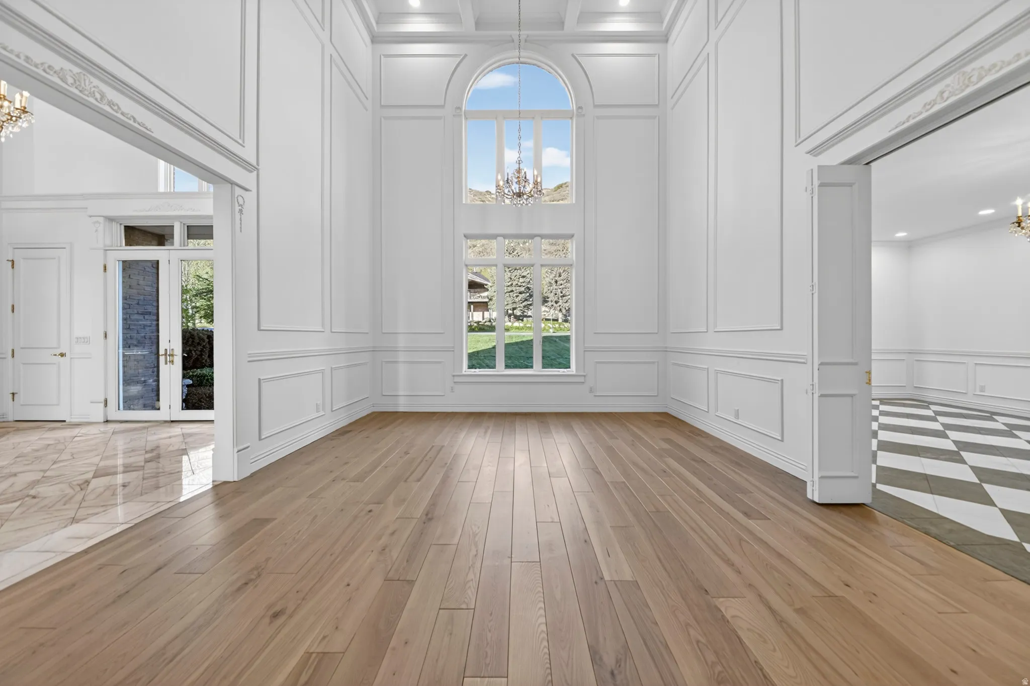 Parlor featuring chandeliers, a decorative wall, french doors, hardwood floors, and a high ceiling