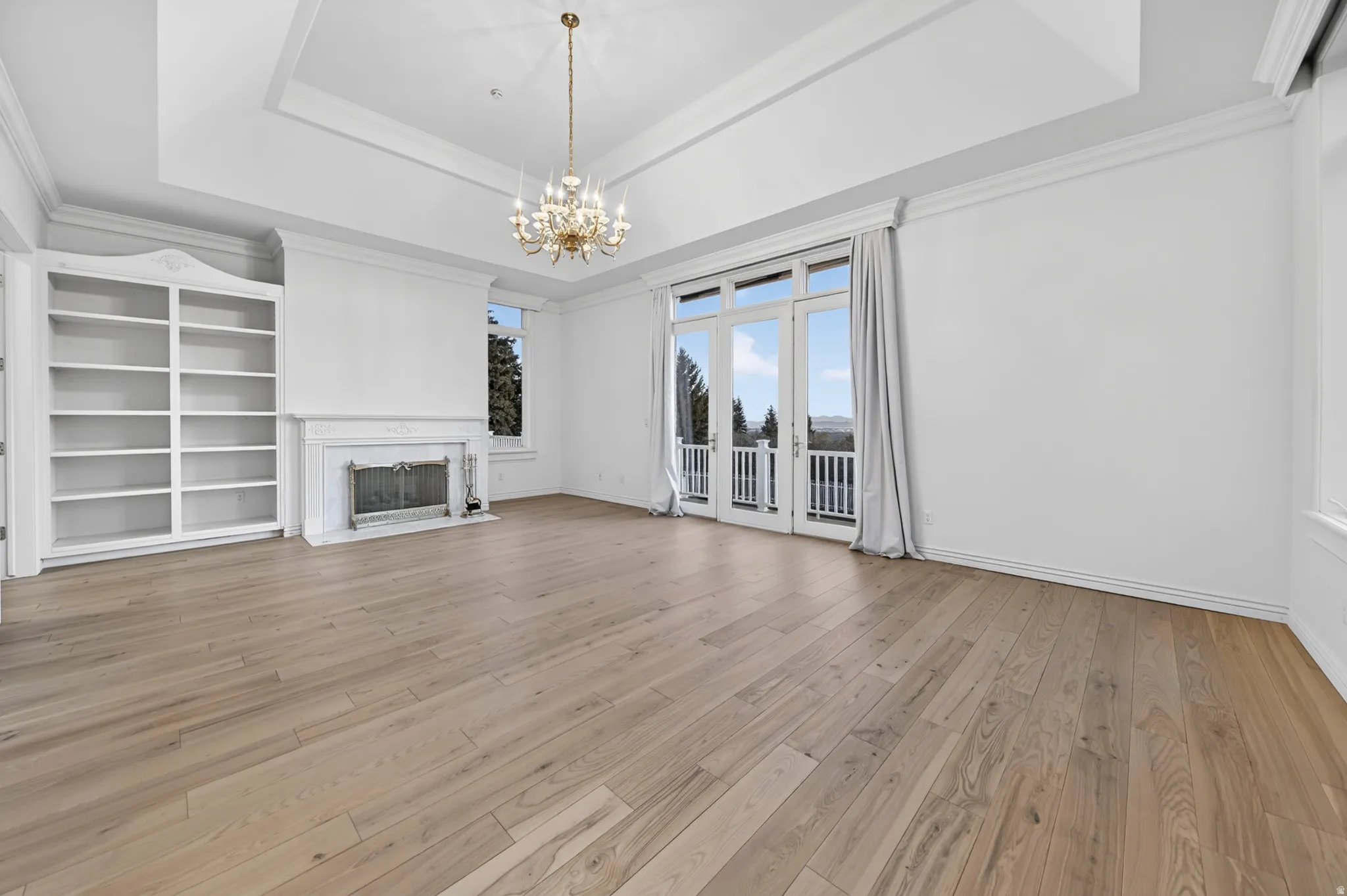 Primary suite with a fireplace, chandelier, crown molding, hardwood flooring, and a tray ceiling