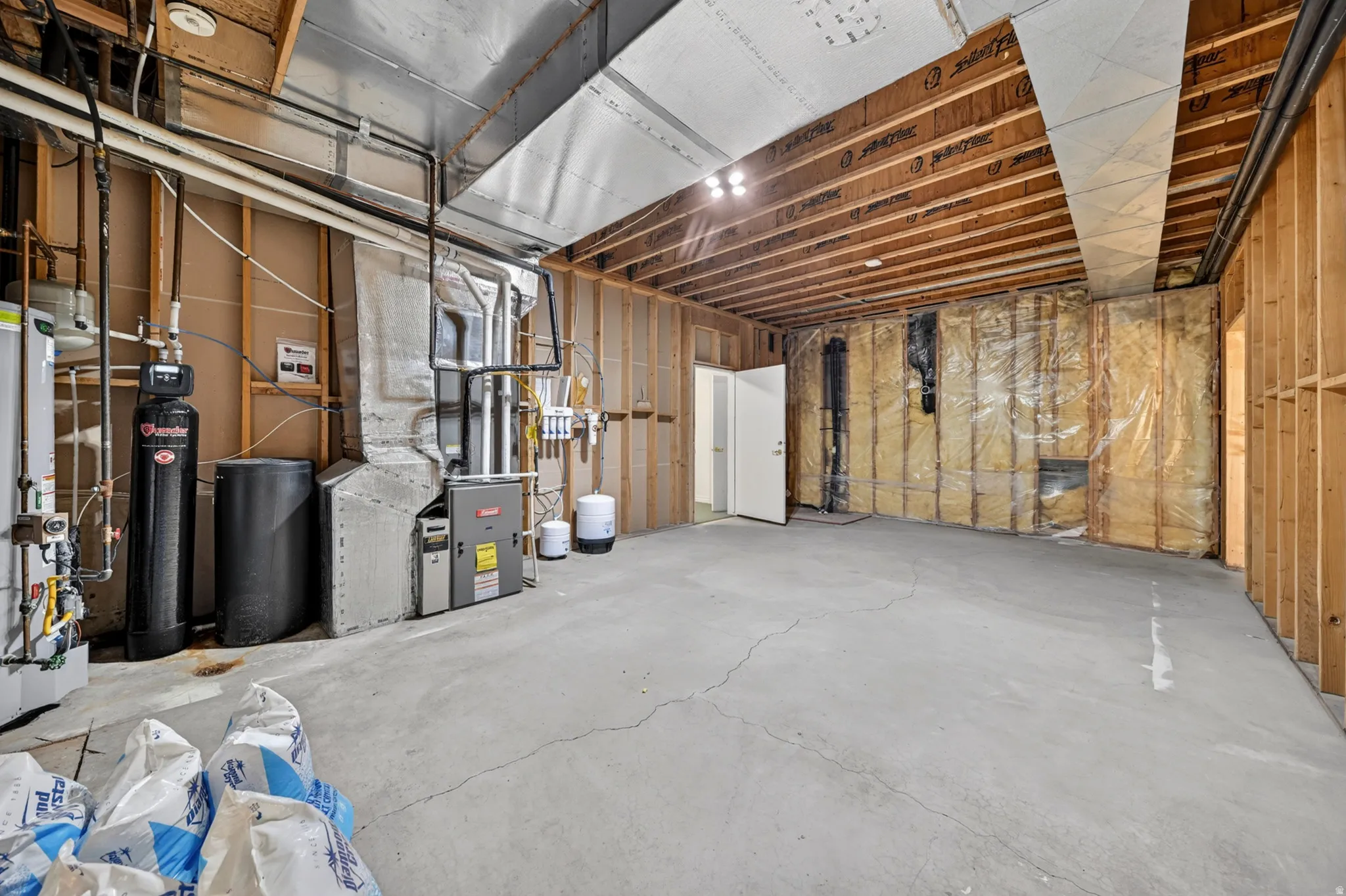Unfinished basement area featuring a water softener, heating unit, and gas water heater