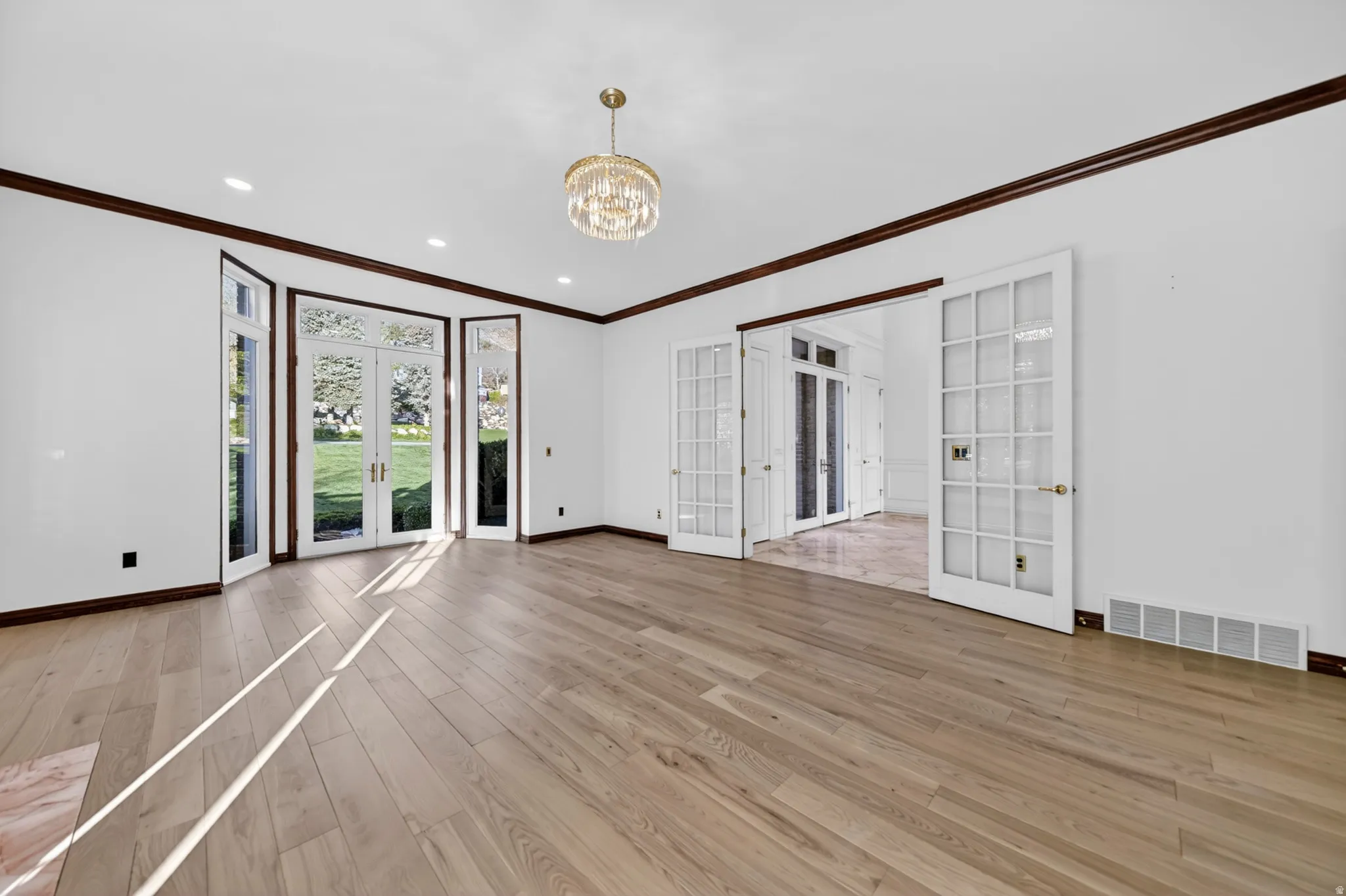 Study featuring french doors, crown molding, hardwood flooring, and chandelier