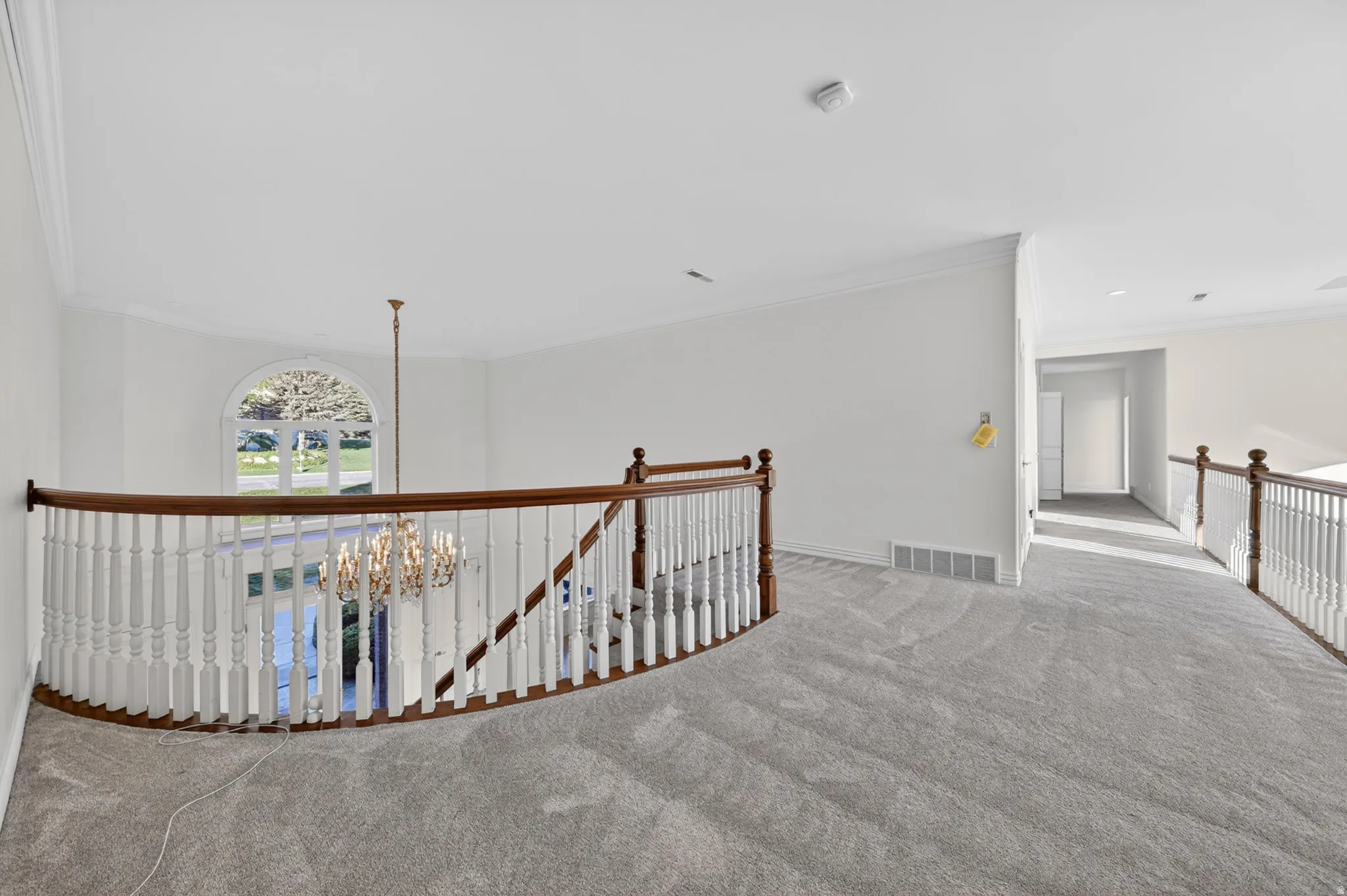 Corridor featuring an upstairs landing, light colored carpet, crown molding, and chandelier