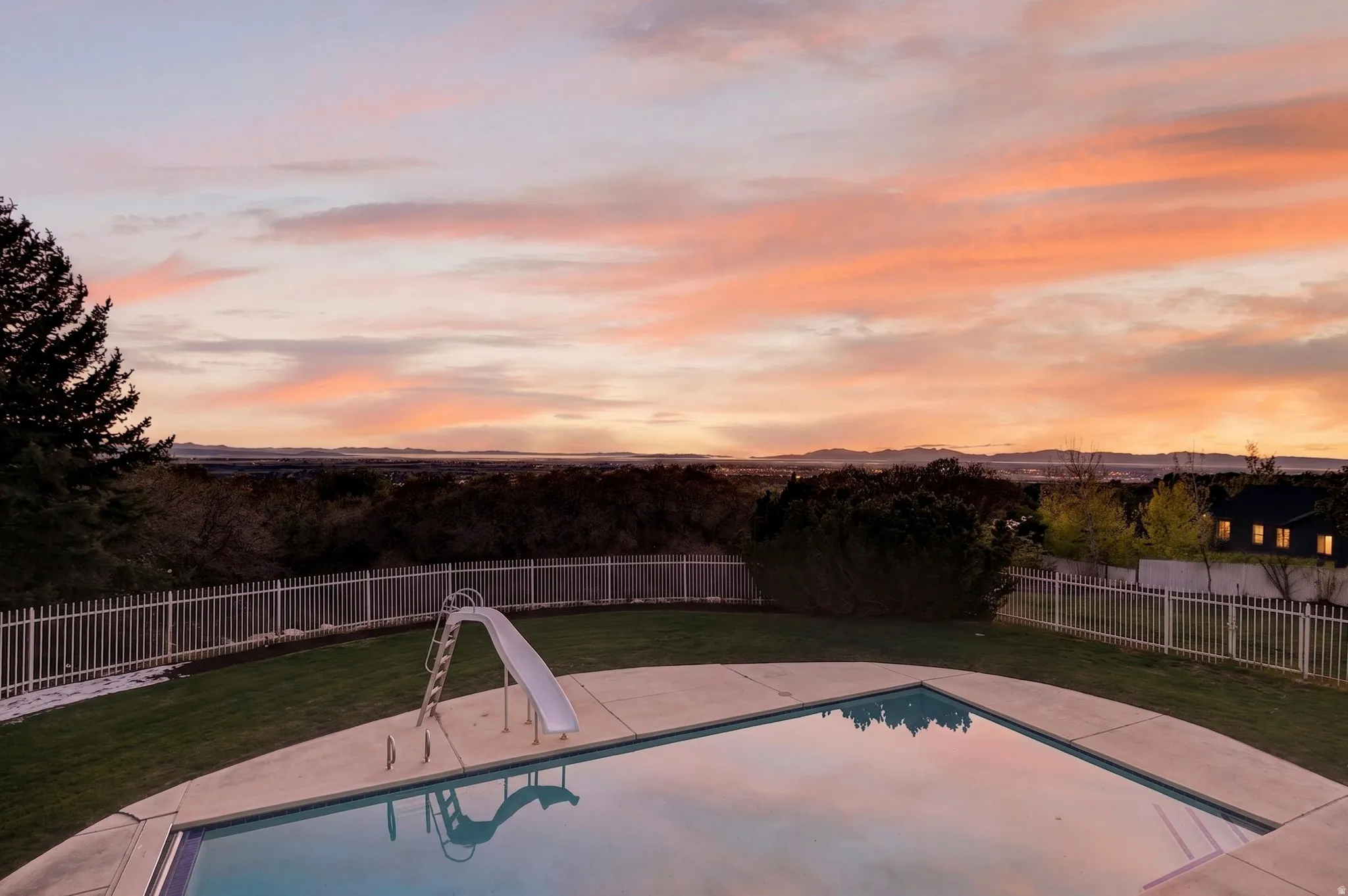Pool at dusk with a fenced backyard, a patio, and a water slide
