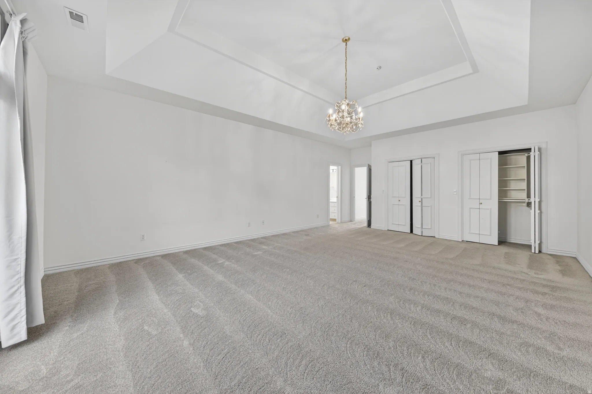Bedroom featuring two closets, chandelier, light colored carpet, and a tray ceiling