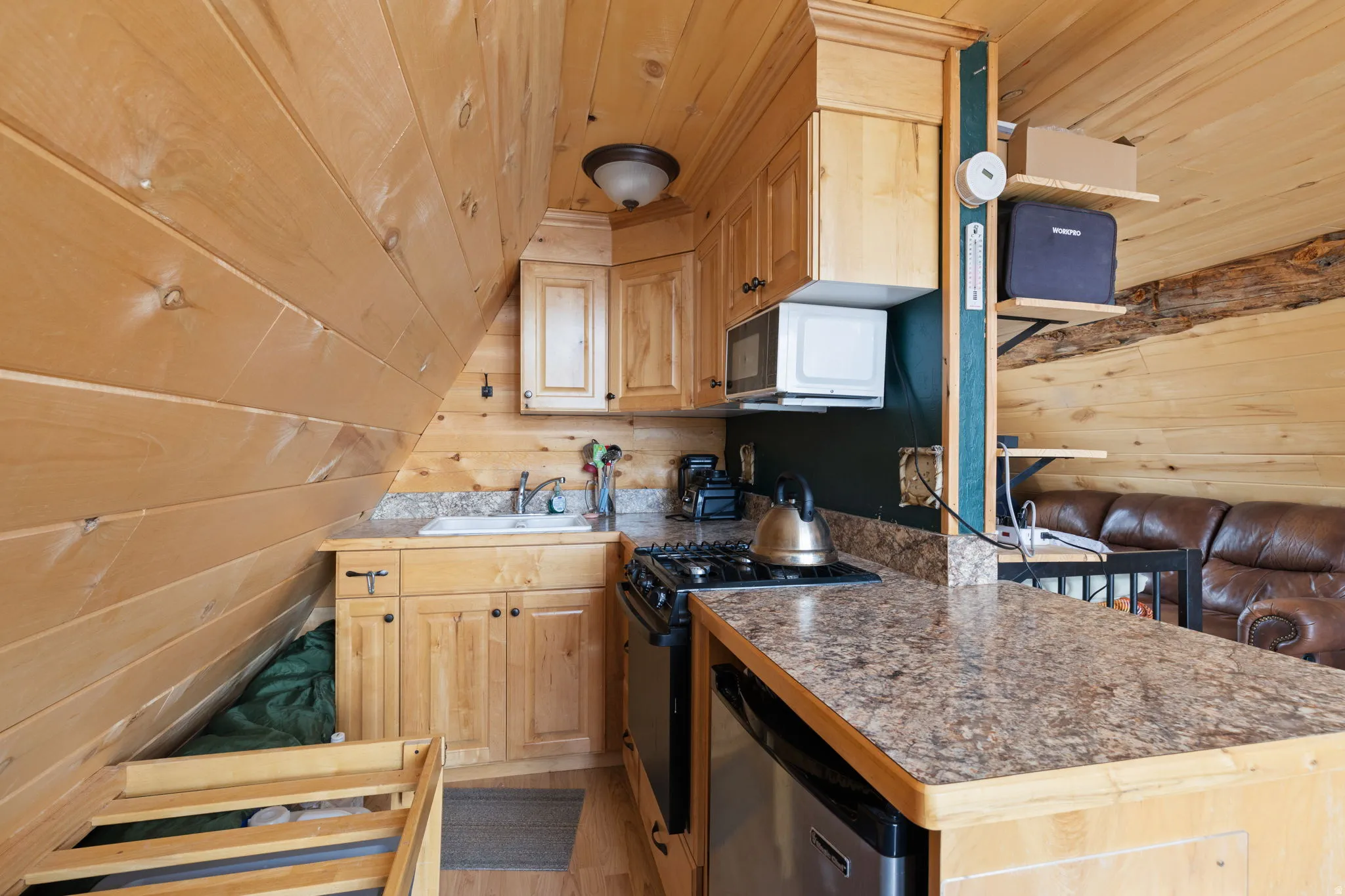 Kitchen with wood walls, wooden ceiling, gas range oven, light wood finished floors, and stainless steel dishwasher