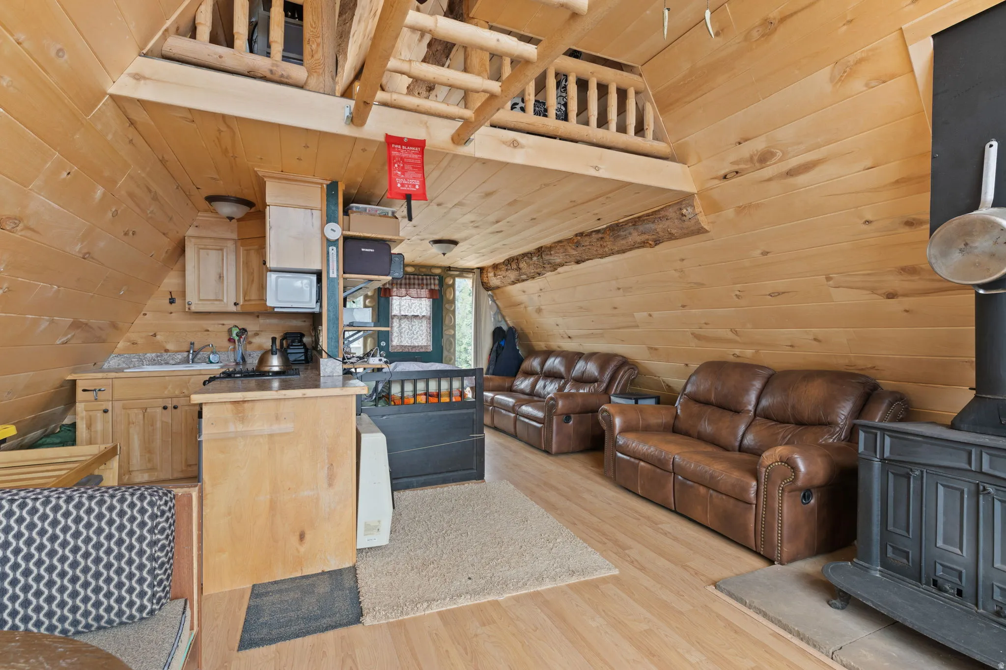 Kitchen with light wood finish cabinetry, wood walls, a vaulted wood ceiling, a wood stove, and light wood-style flooring