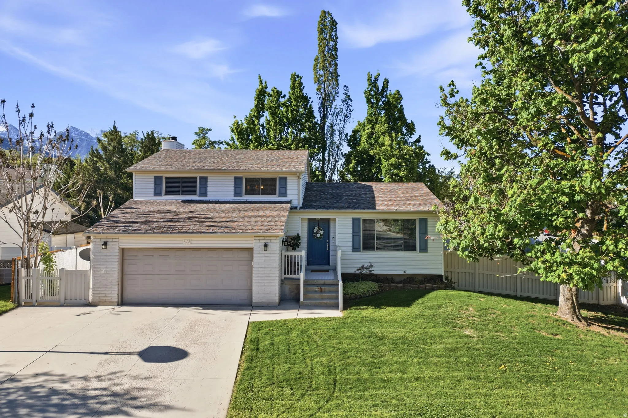 Tri-level home with concrete driveway, an attached garage, roof with shingles, brick siding, and a chimney