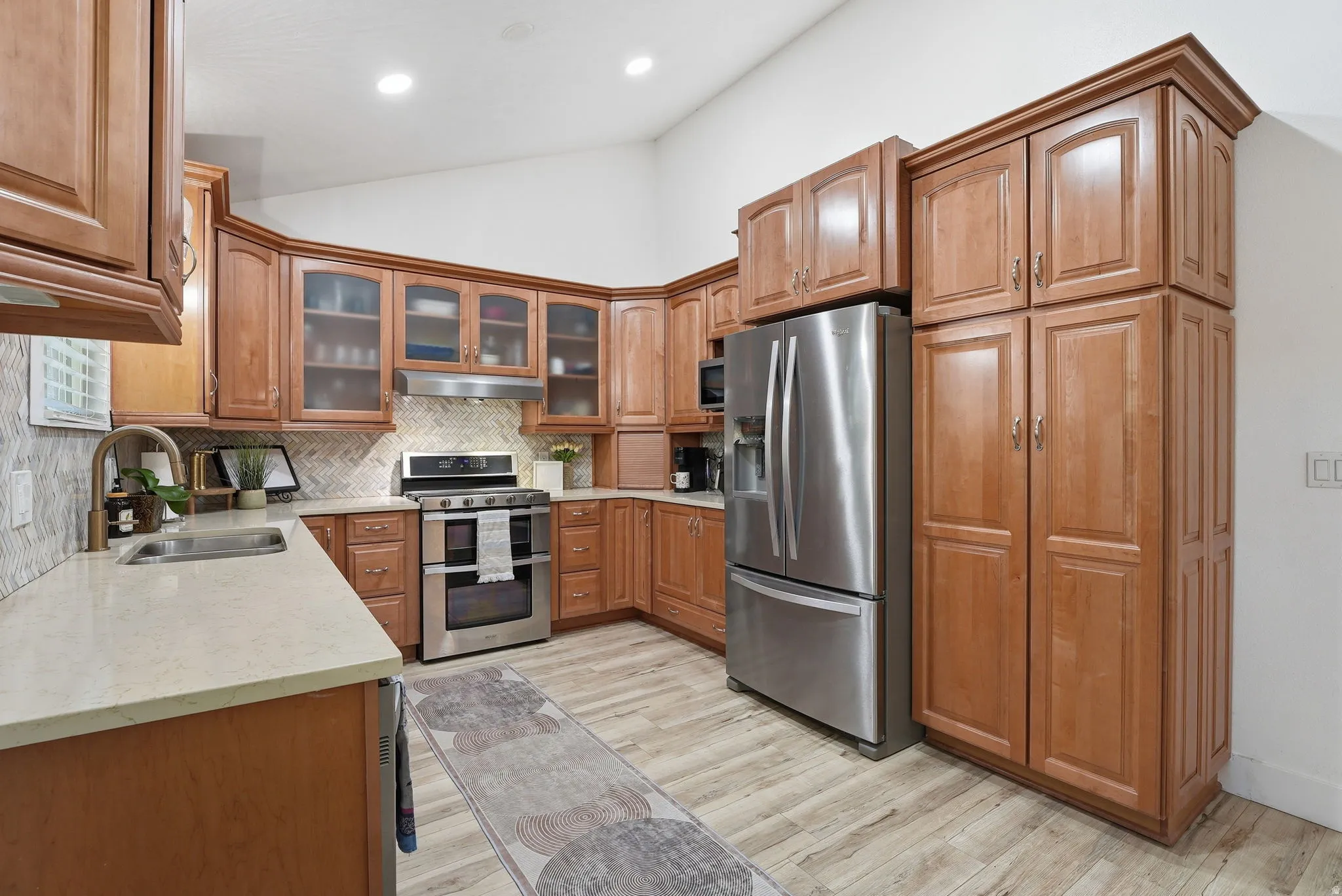 Kitchen with wood finish cabinetry, lofted ceiling, glass insert cabinets, stainless steel appliances, and backsplash