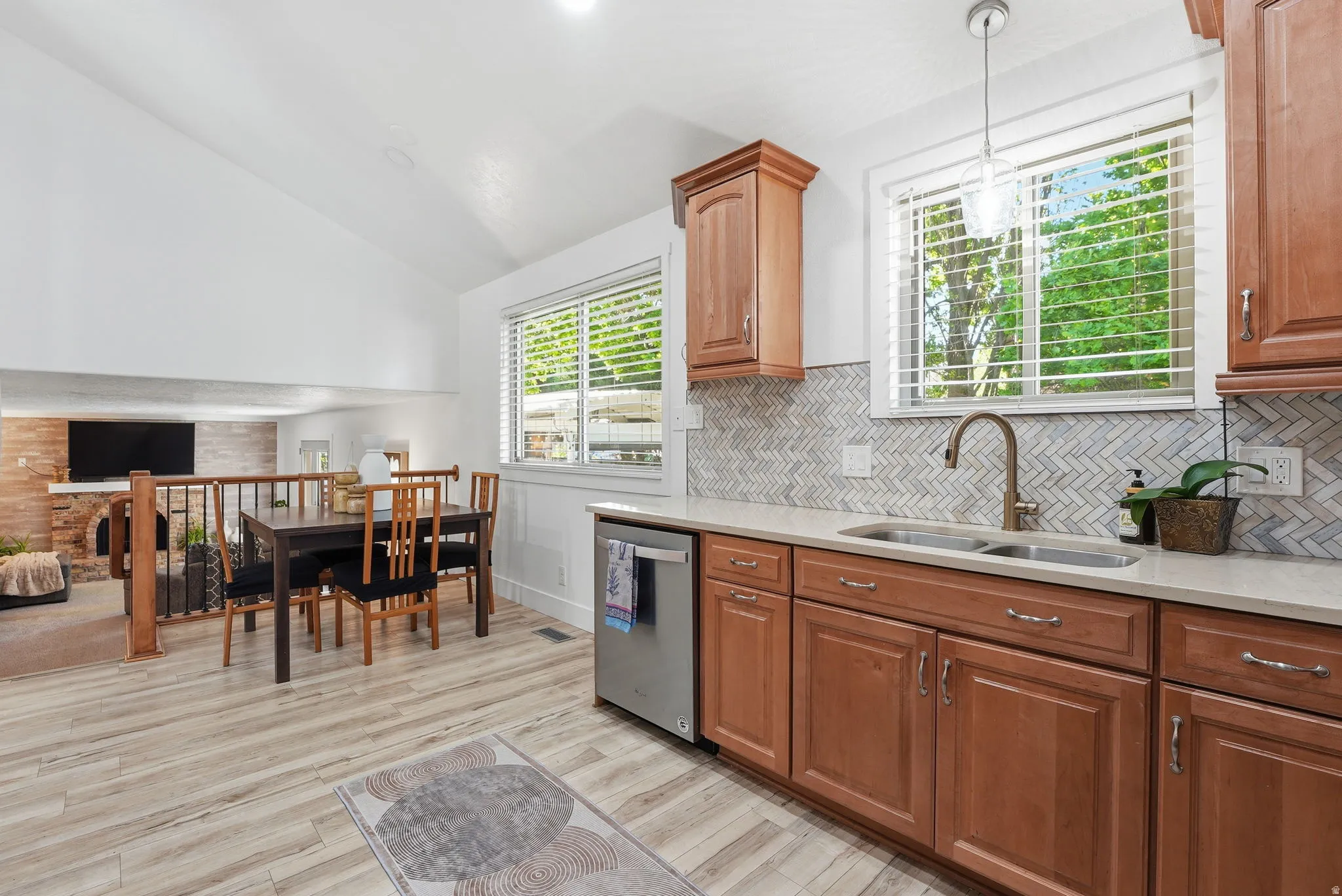 Kitchen with light stone counters, wood finish cabinetry, vaulted ceiling, light wood-style flooring, and stainless steel dishwasher