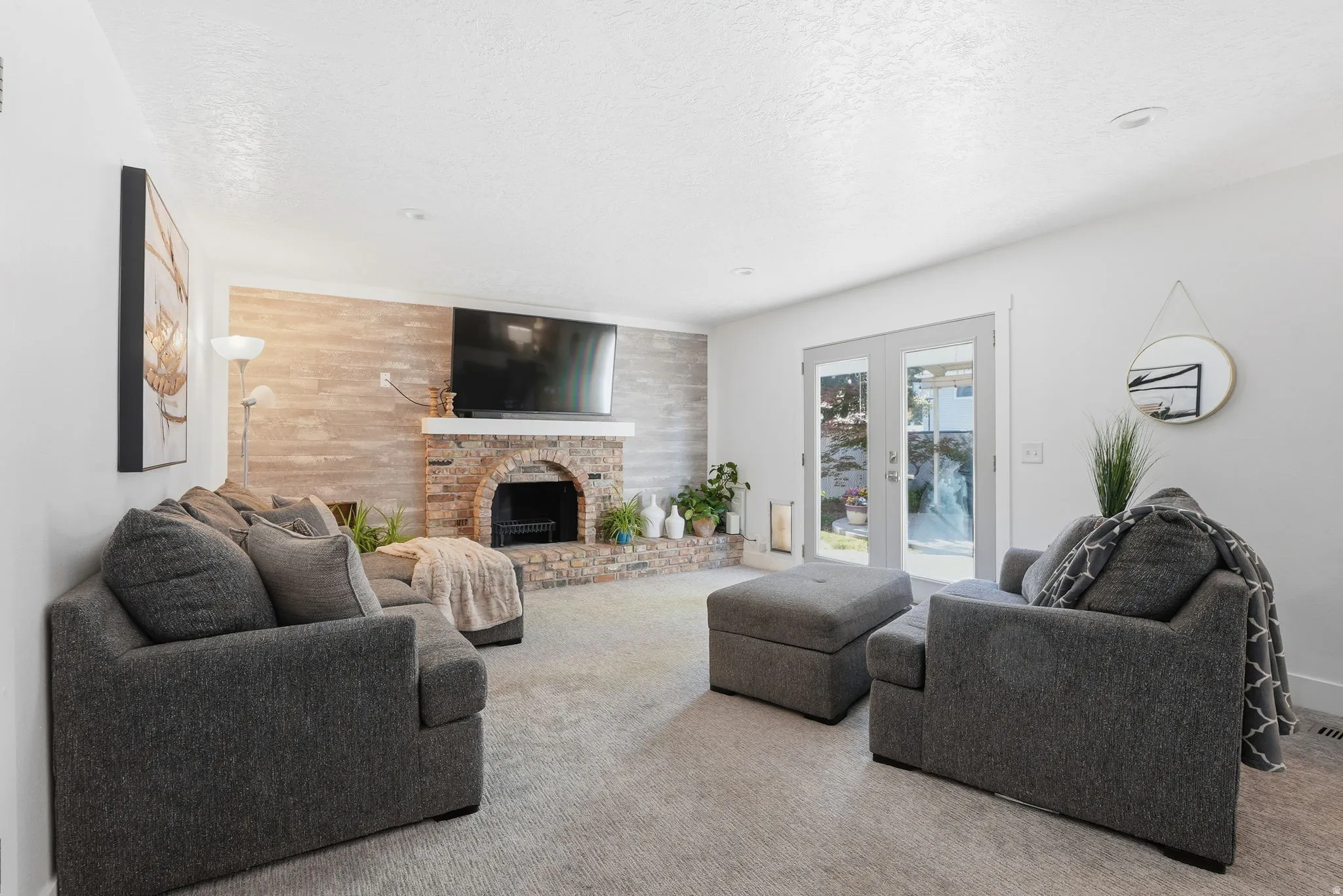Carpeted living area with wooden walls, a brick fireplace, a textured ceiling, french doors, and an accent wall