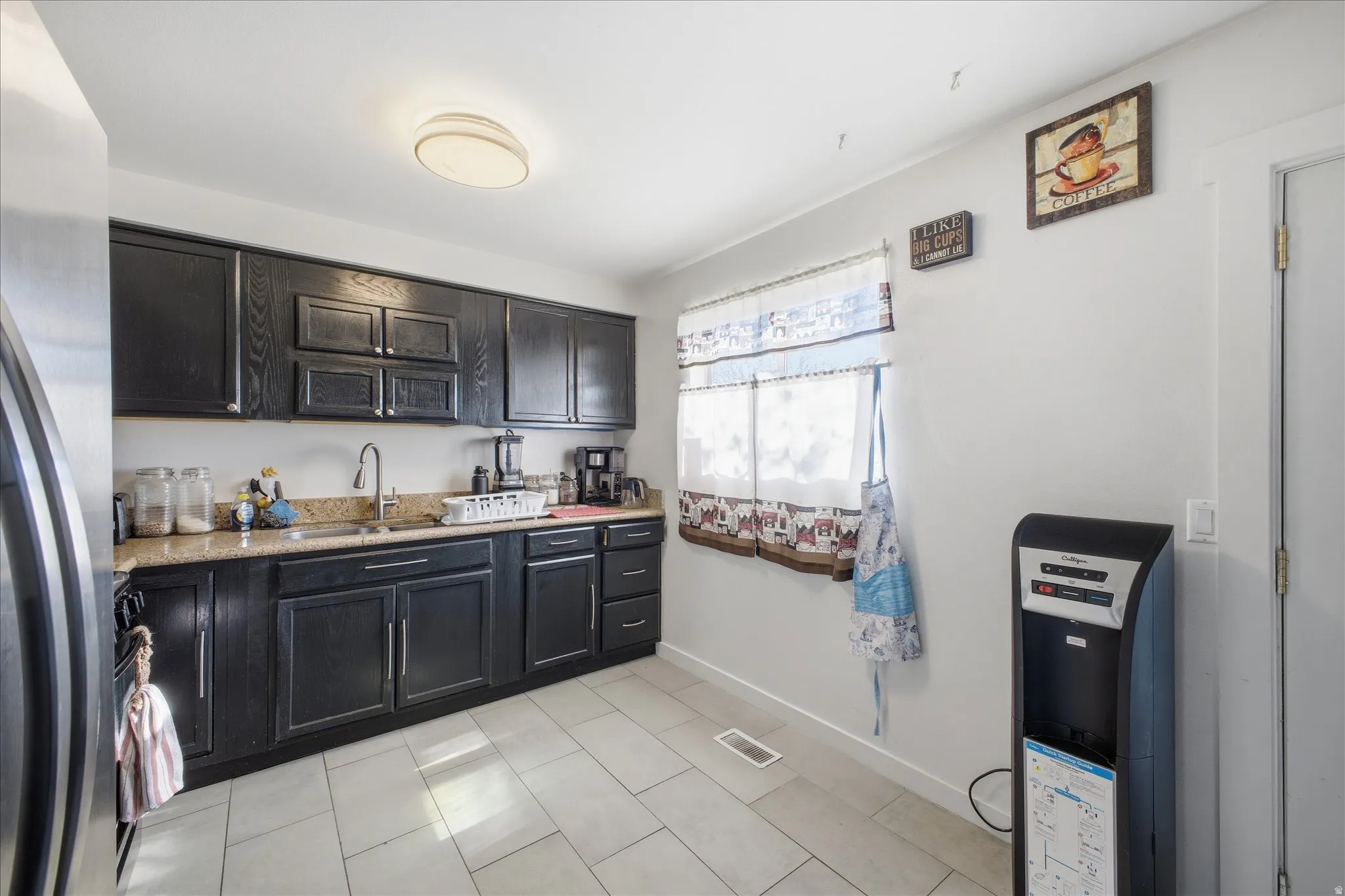 Kitchen with refrigerator, dark cabinets, light  counters, and light tile patterned floors
