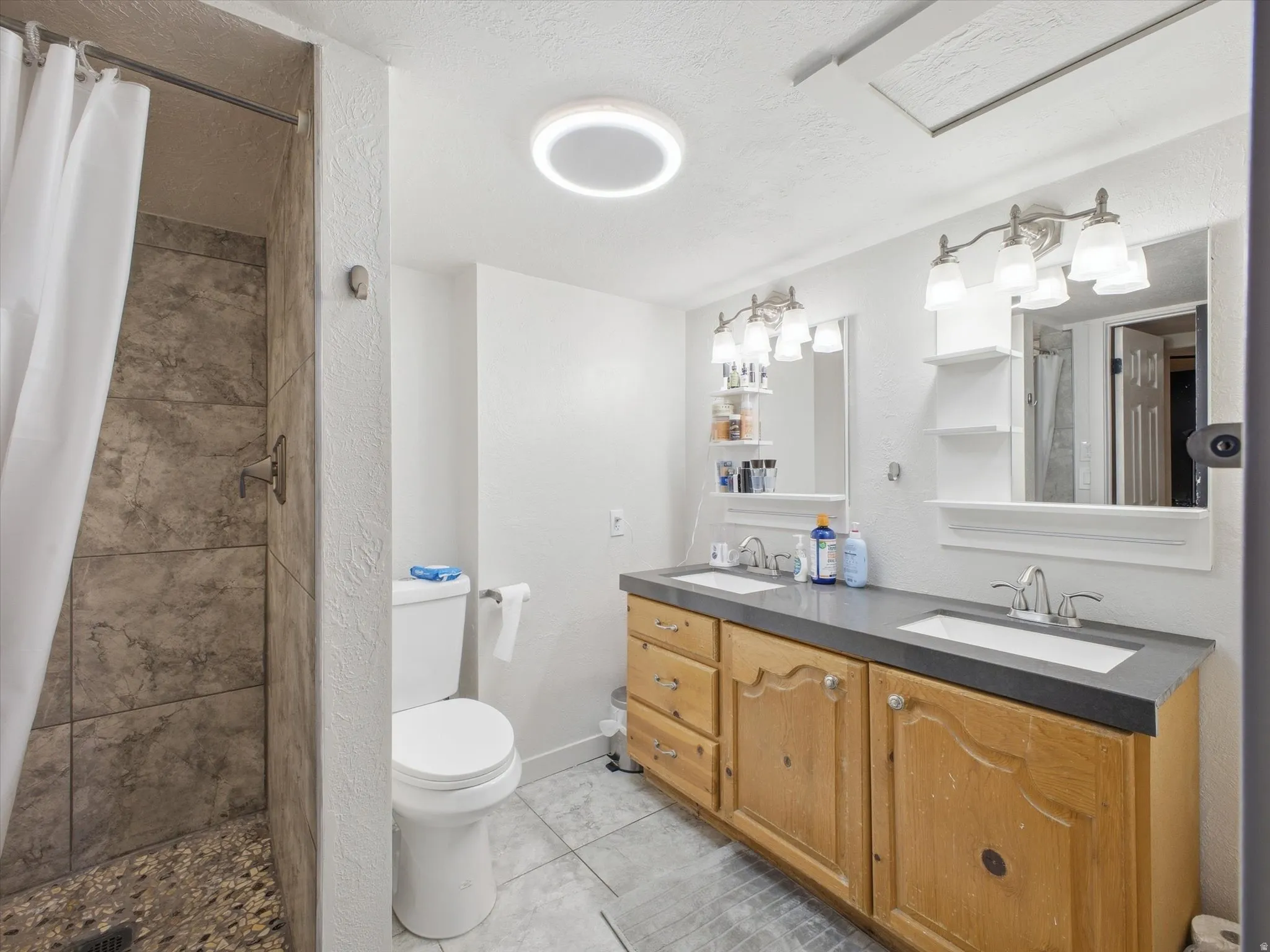 Bathroom featuring double vanity, a stall shower, light tile patterned flooring, and a textured wall
