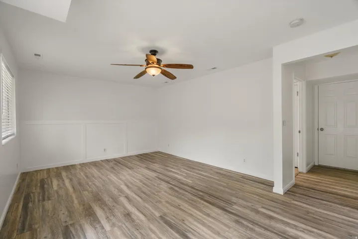 Empty room featuring dark wood-type flooring, ceiling fan, a decorative wall, and a wainscoted wall