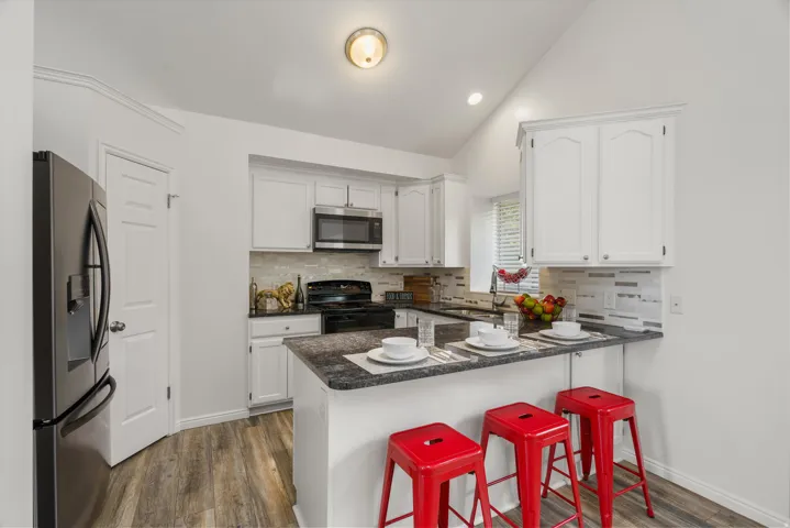 Kitchen with a kitchen breakfast bar, lofted ceiling, white cabinets, a peninsula, and stainless steel appliances