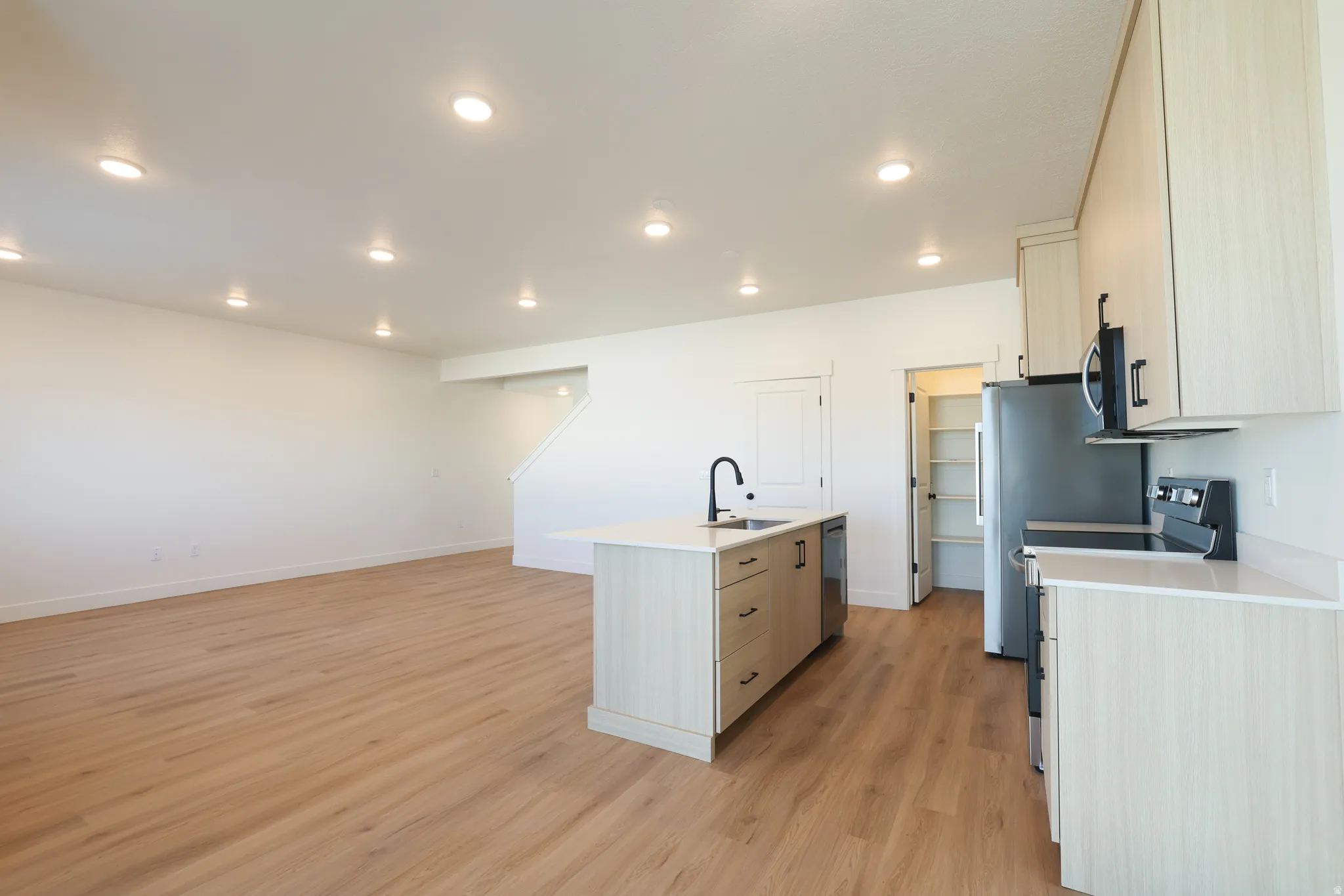 Kitchen featuring stainless steel appliances, a kitchen island with sink, light wood finished floors, recessed lighting, and light wood finish cabinetry