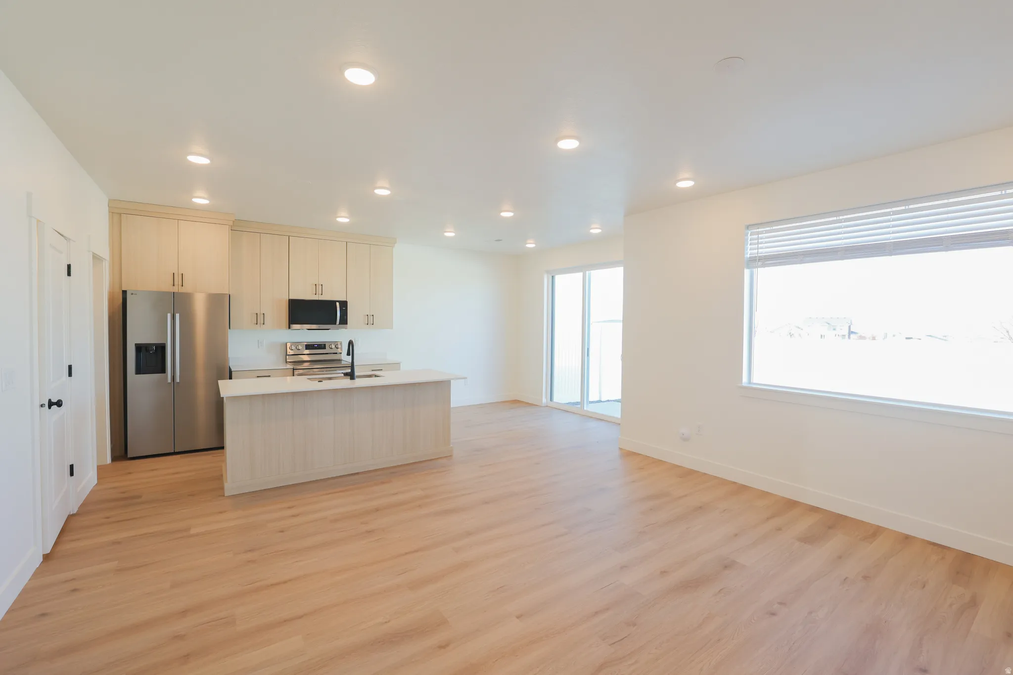 Kitchen featuring stainless steel appliances, a kitchen island with sink, recessed lighting, light countertops, and light wood-type flooring