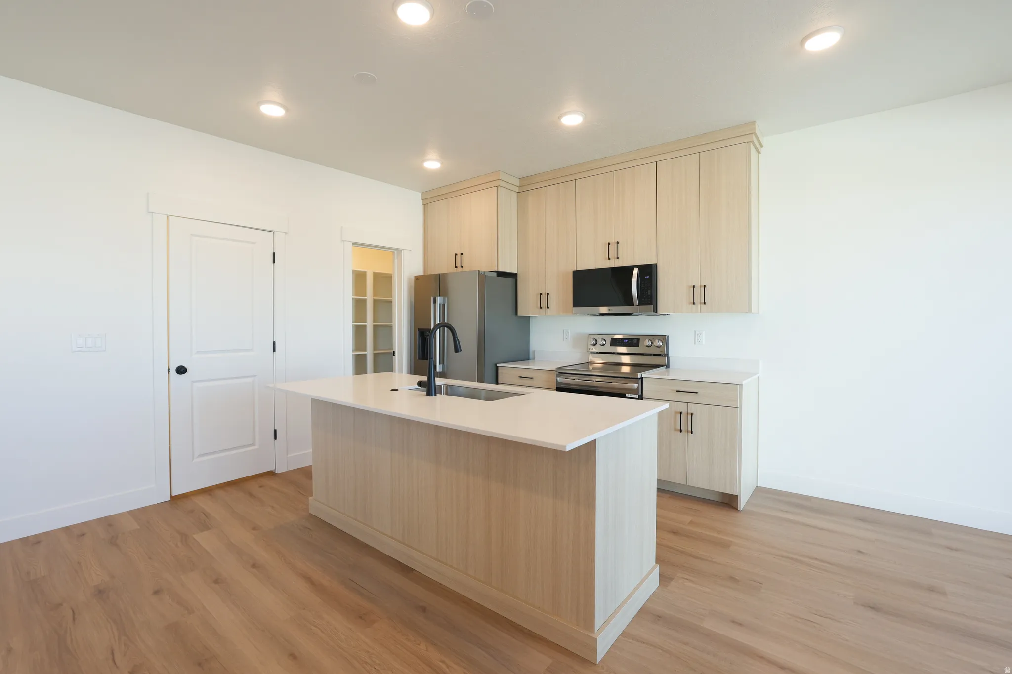 Kitchen with stainless steel appliances, light wood finish cabinets, a center island with sink, light wood-style floors, and recessed lighting