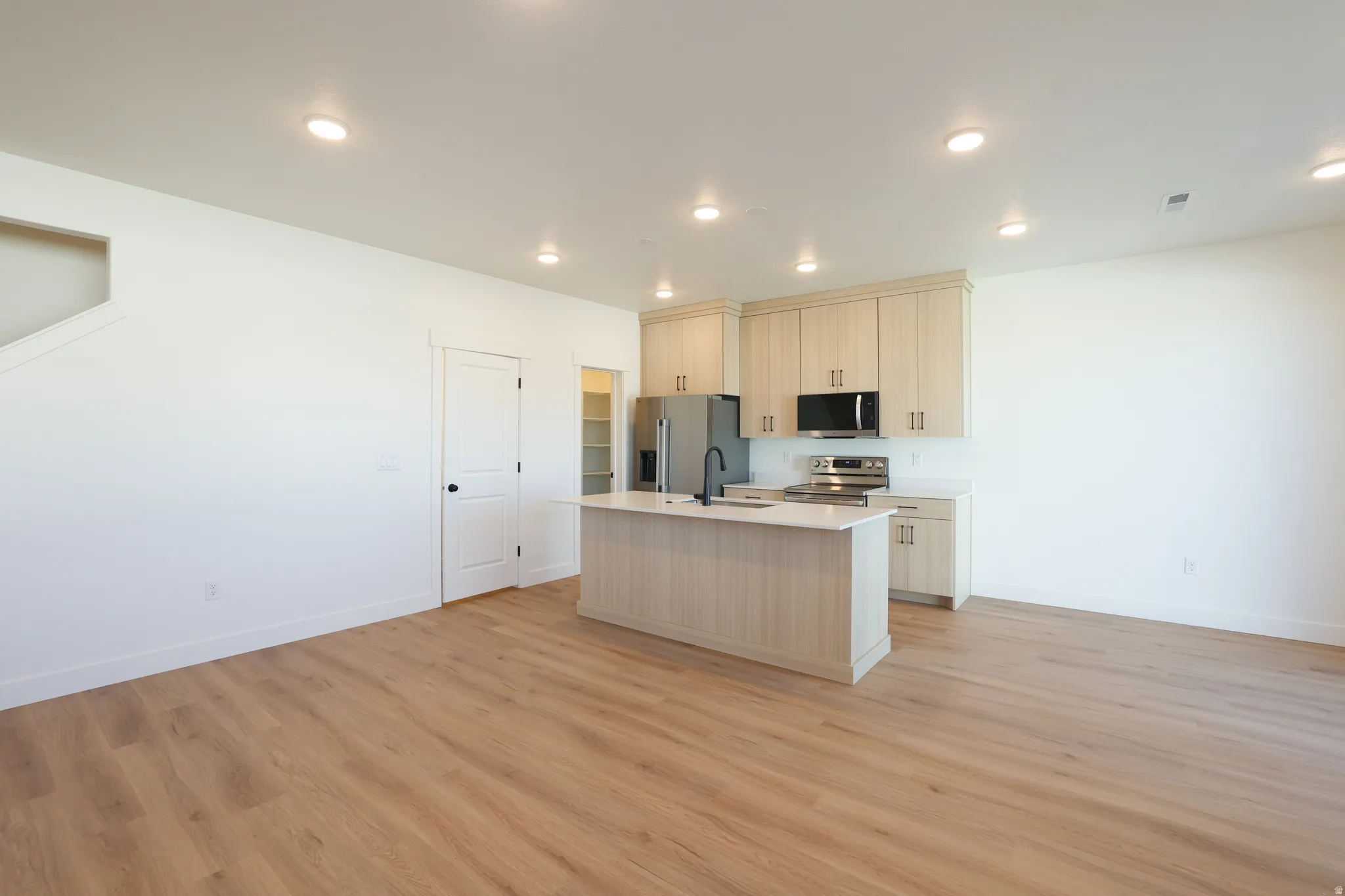 Kitchen with an island with sink, stainless steel appliances, open floor plan, light wood-type flooring, and recessed lighting