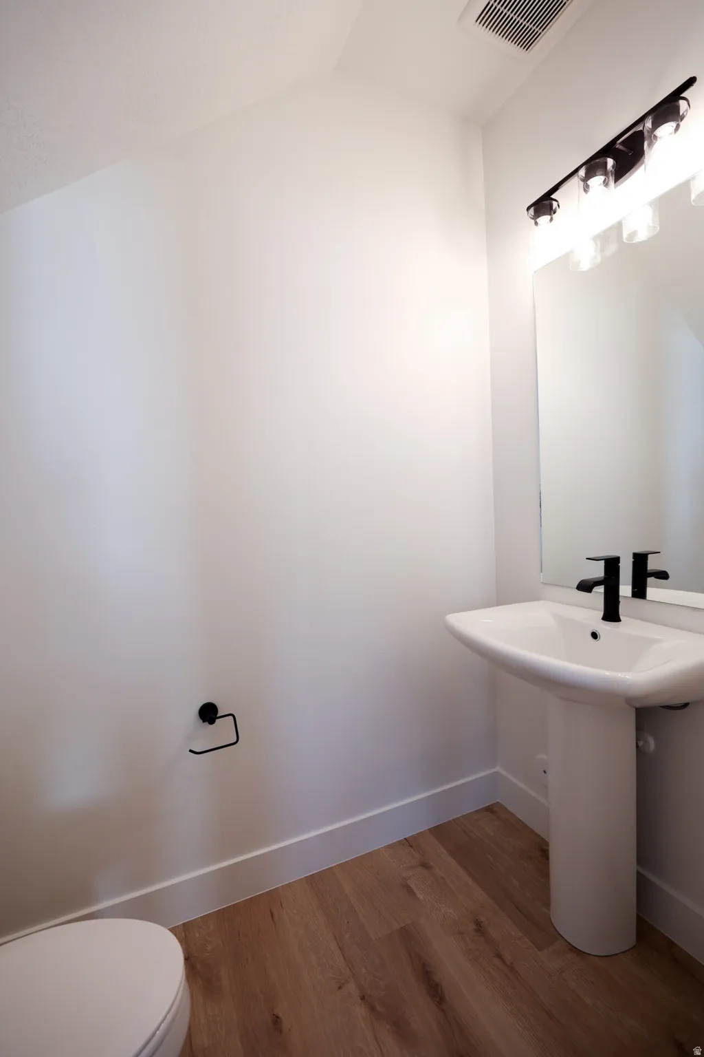 Half bath with dark wood-style floors and vaulted ceiling