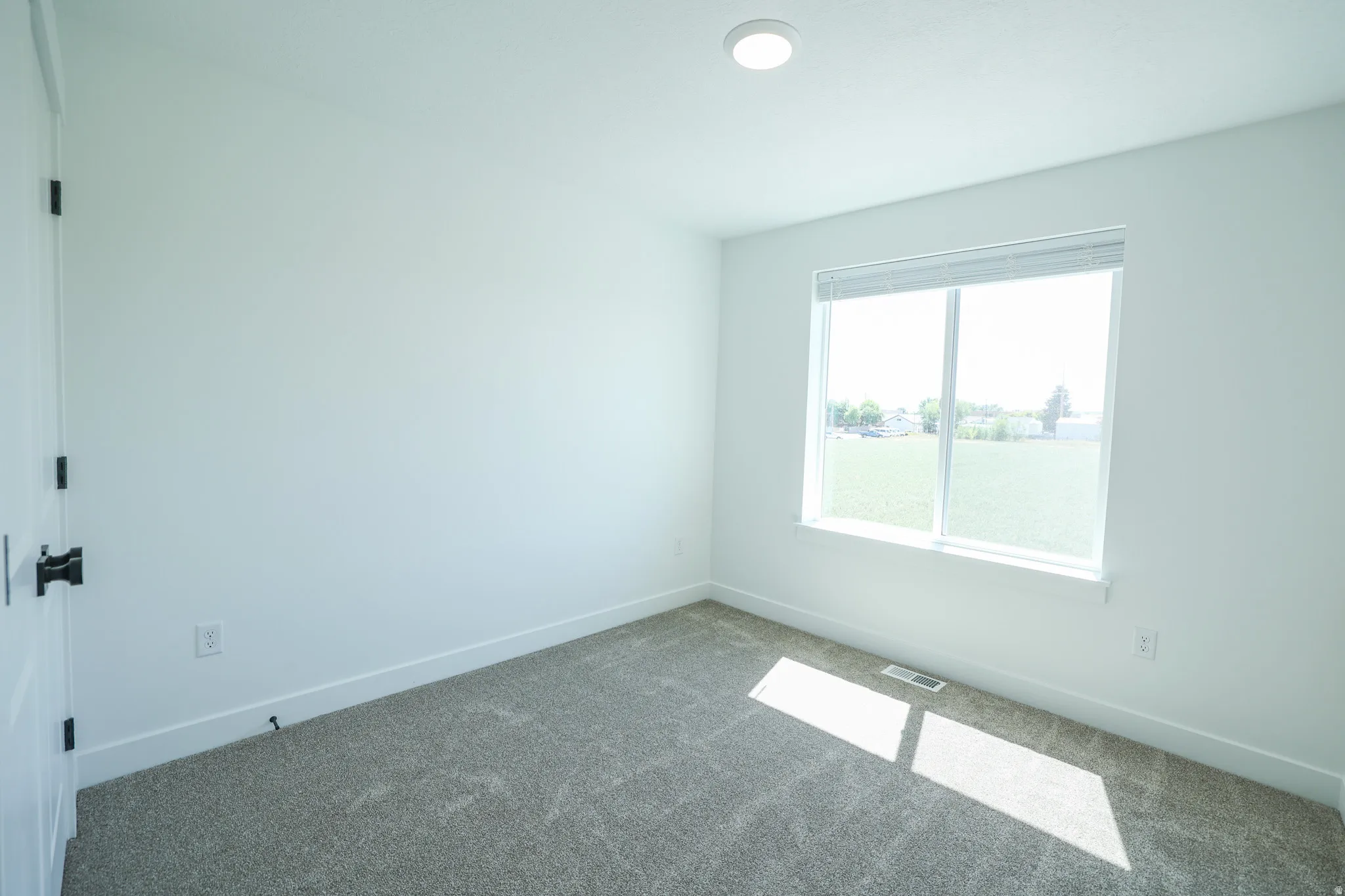 Light-filled room featuring a large window, recessed ceiling lighting, and soft gray carpeting