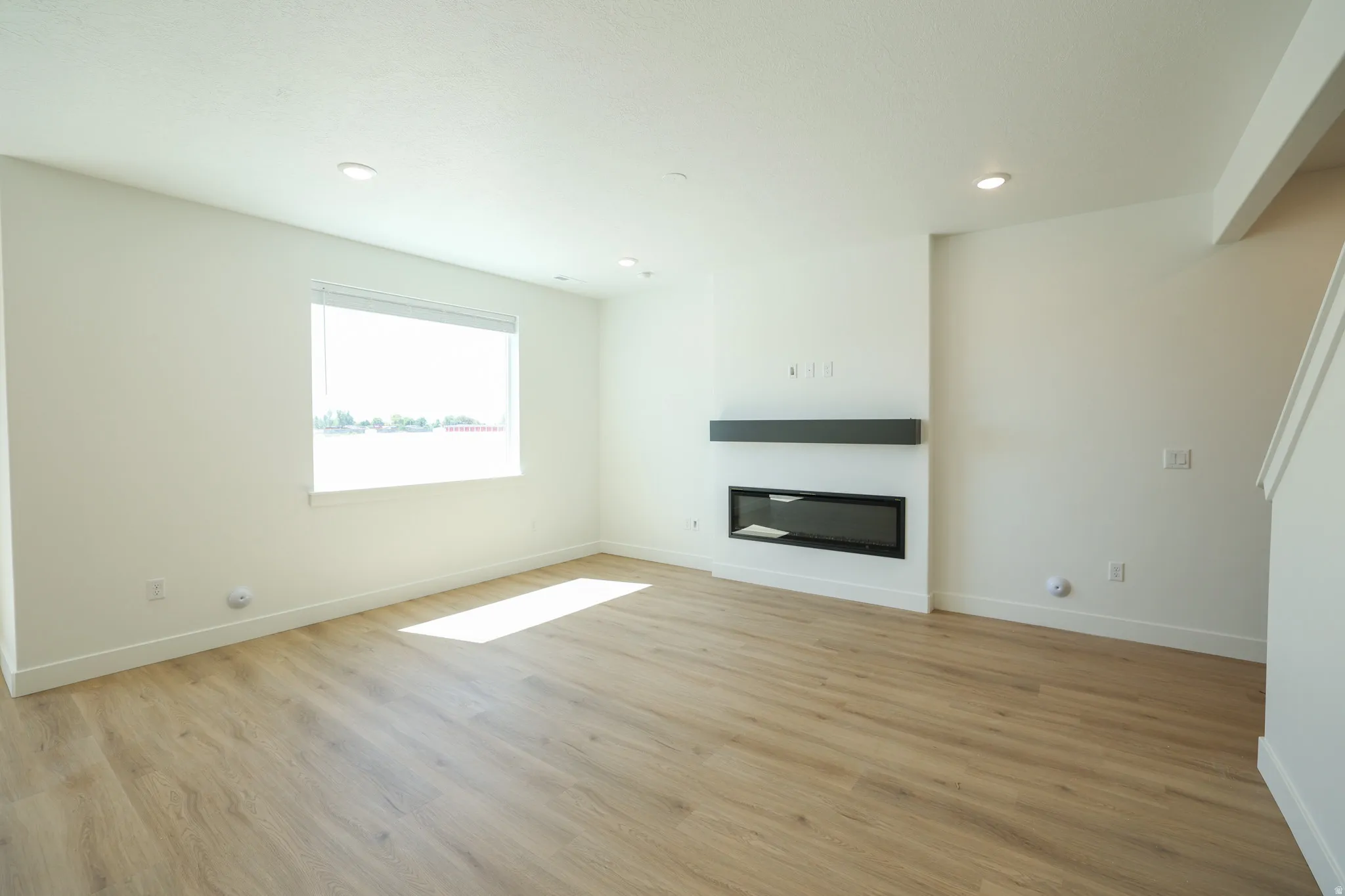 Recessed lighting, wood-finish flooring, and a linear electric fireplace with a dark mantel