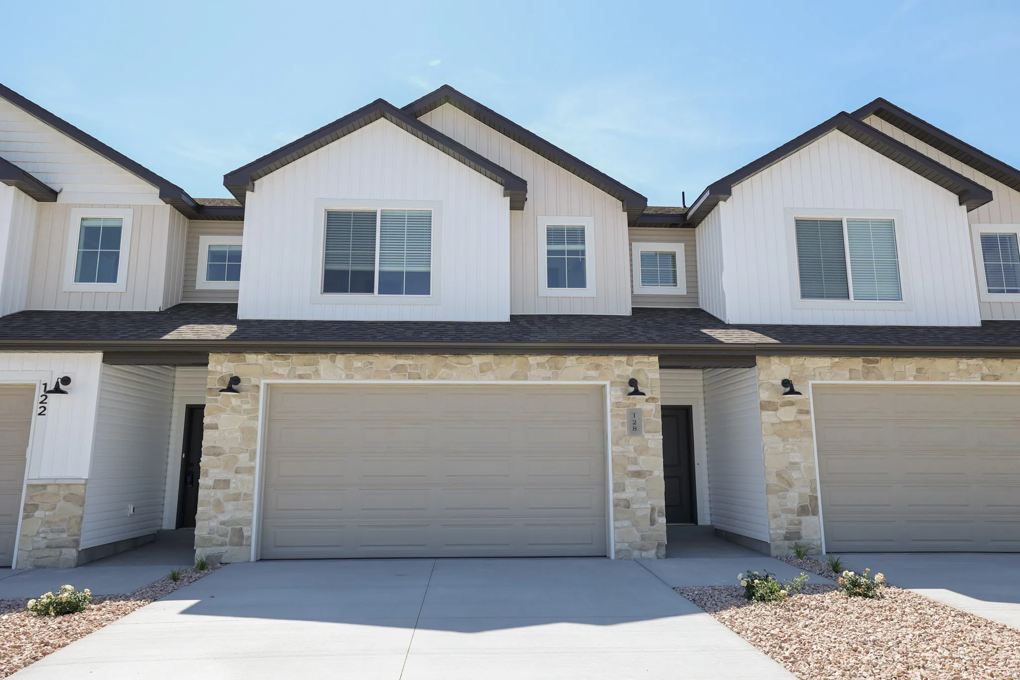 Contemporary exterior with vertical white siding, stone veneer accents, dark shingle roofing, and attached garage