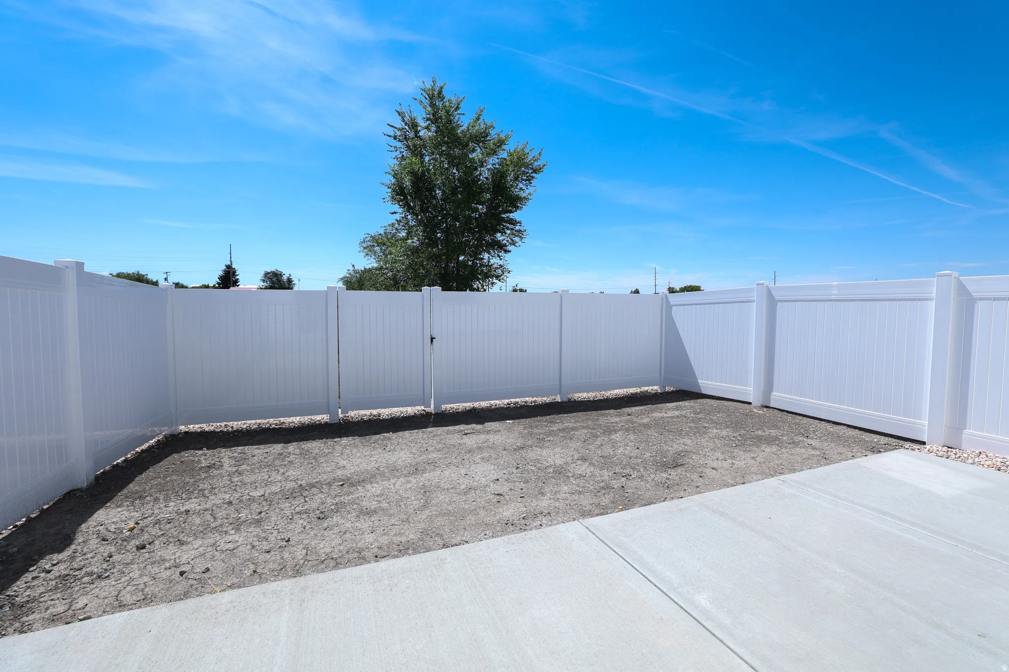 Fenced yard area featuring a white vinyl privacy fence with gate and concrete patio