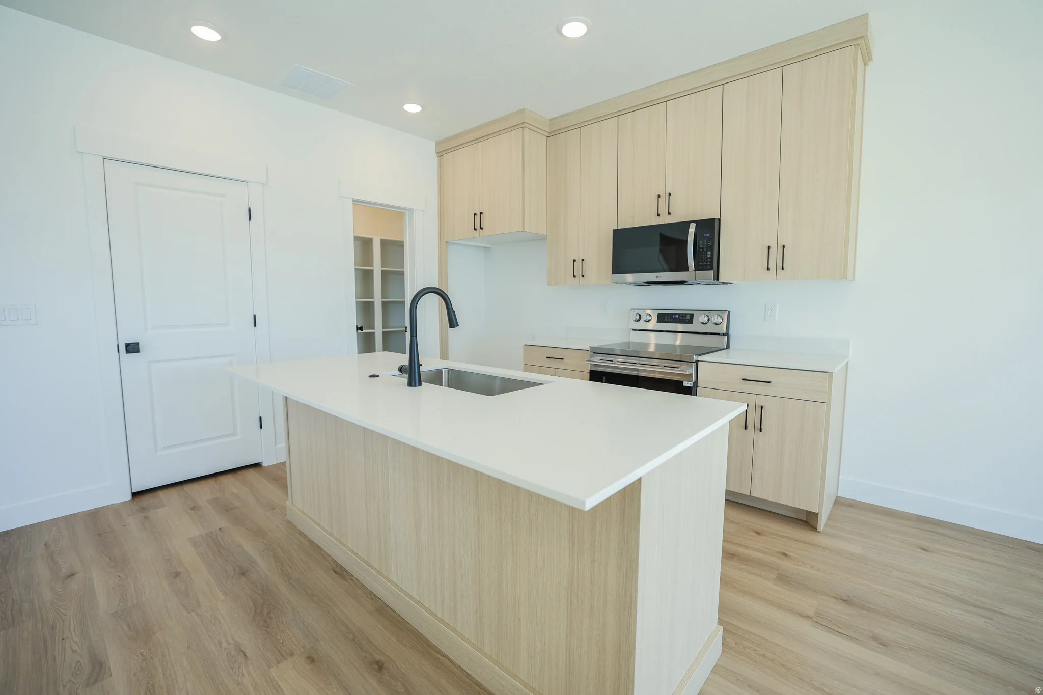 Kitchen featuring an island with a stainless steel sink, light wood-finish cabinetry, stainless steel appliances, and wood-finish flooring