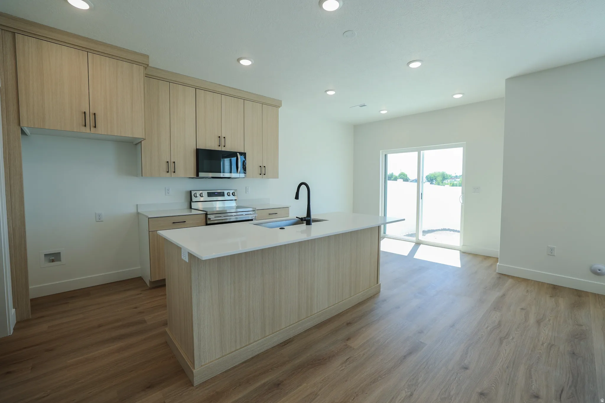 Modern kitchen featuring light wood-finish cabinetry, stainless steel appliances, a center island with a white countertop, and wood-finish flooring