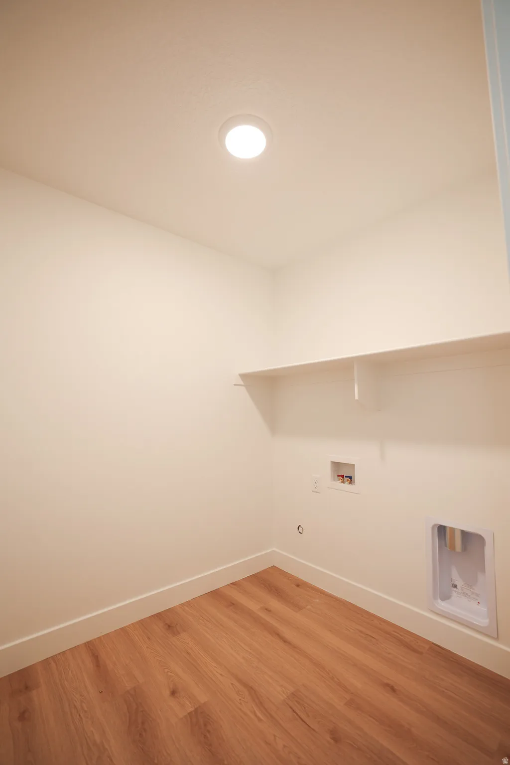 Recessed ceiling light, white walls, built-in shelving, wood-finish flooring, and laundry hookups