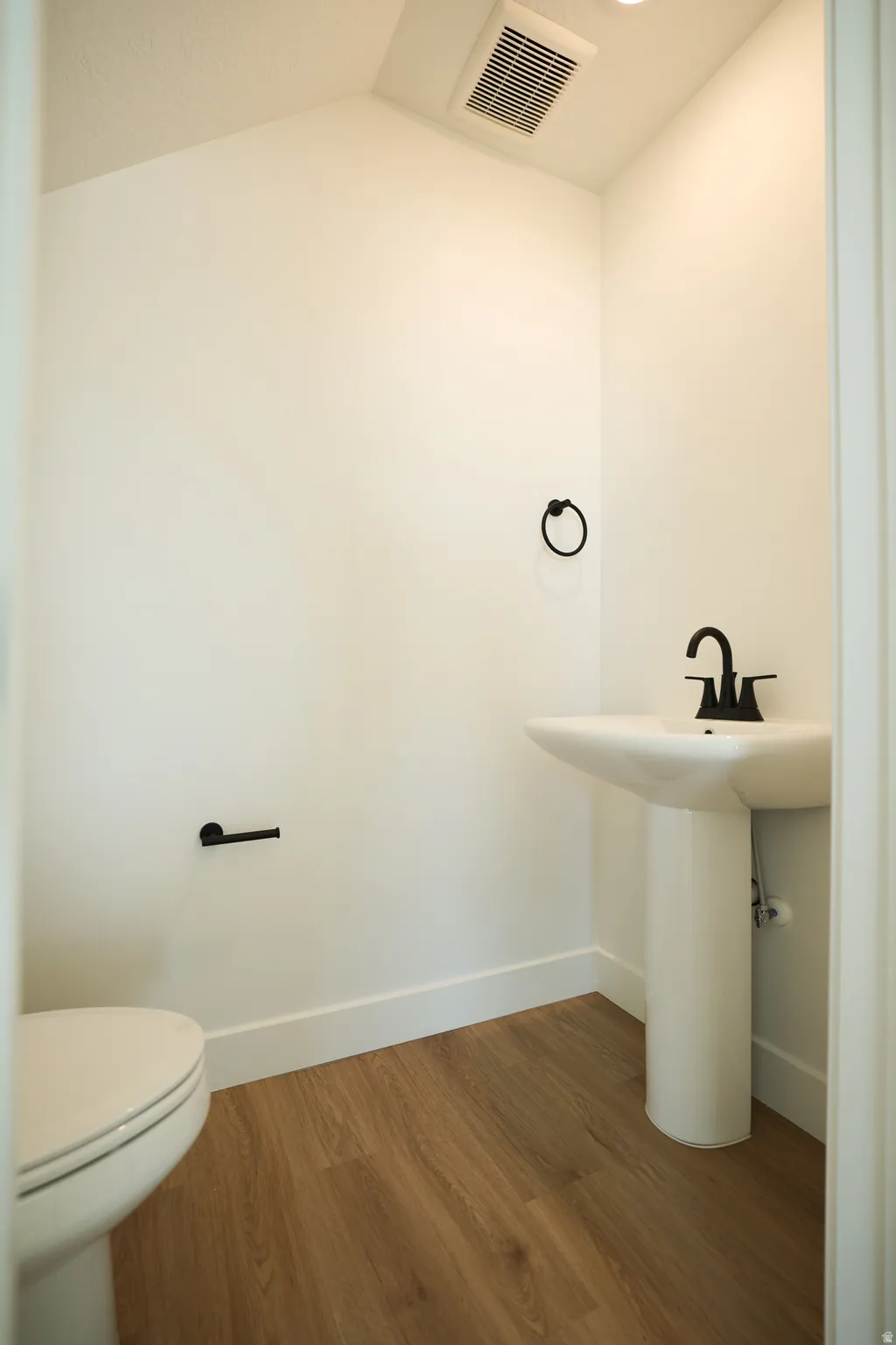 Pedestal sink with a black faucet, wood-finish flooring, and white baseboards