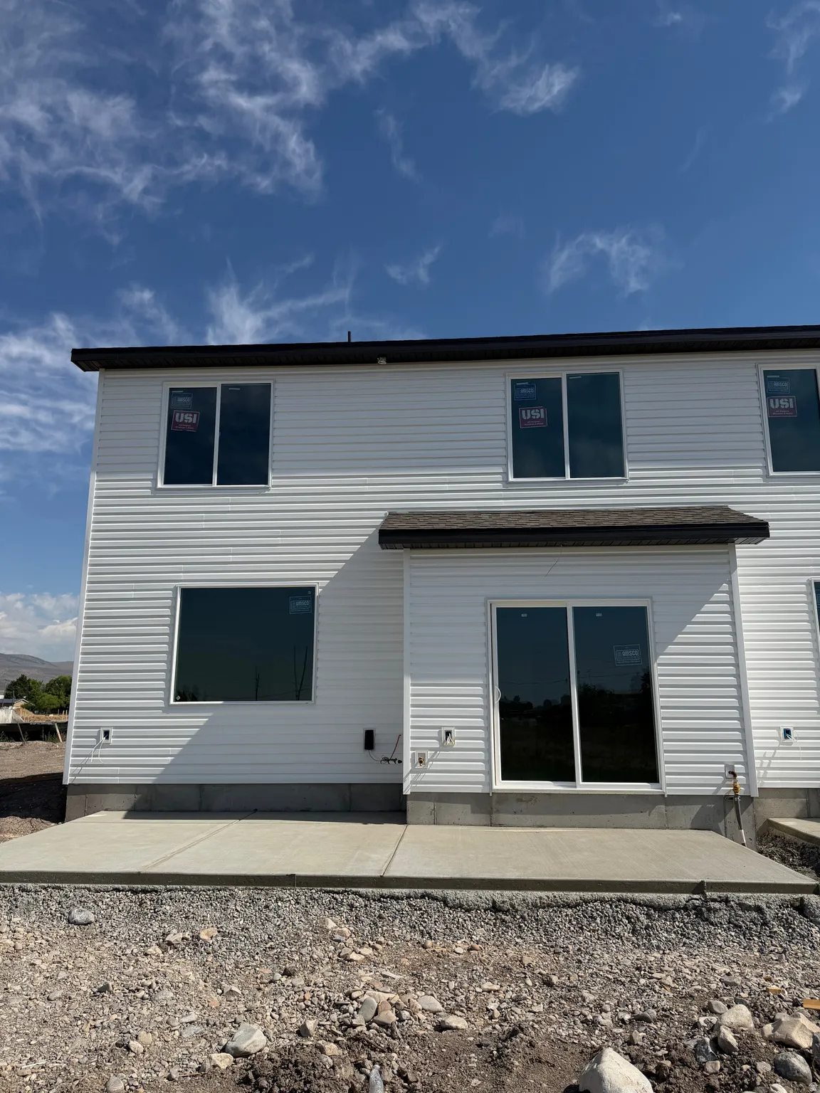 Rear exterior featuring white horizontal siding, a dark shingle roof, and a concrete patio